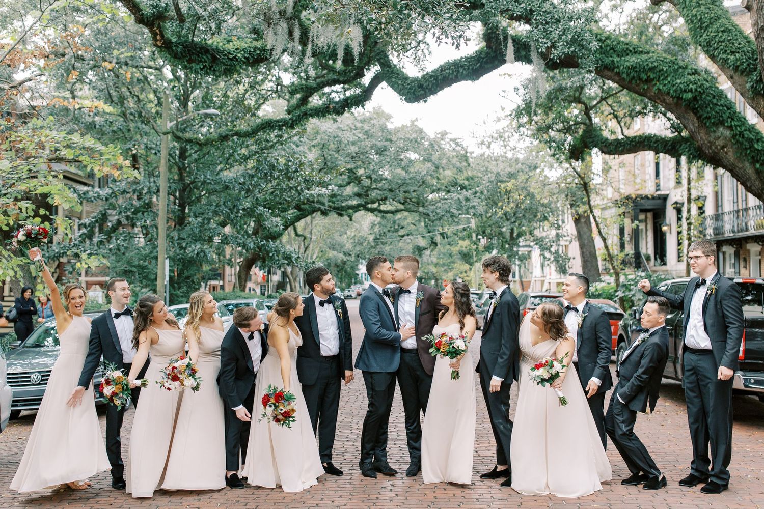 Wedding party poses together on a tree-lined street with Spanish moss hanging overhead in classic formal attire on Jones Street in Savannah.