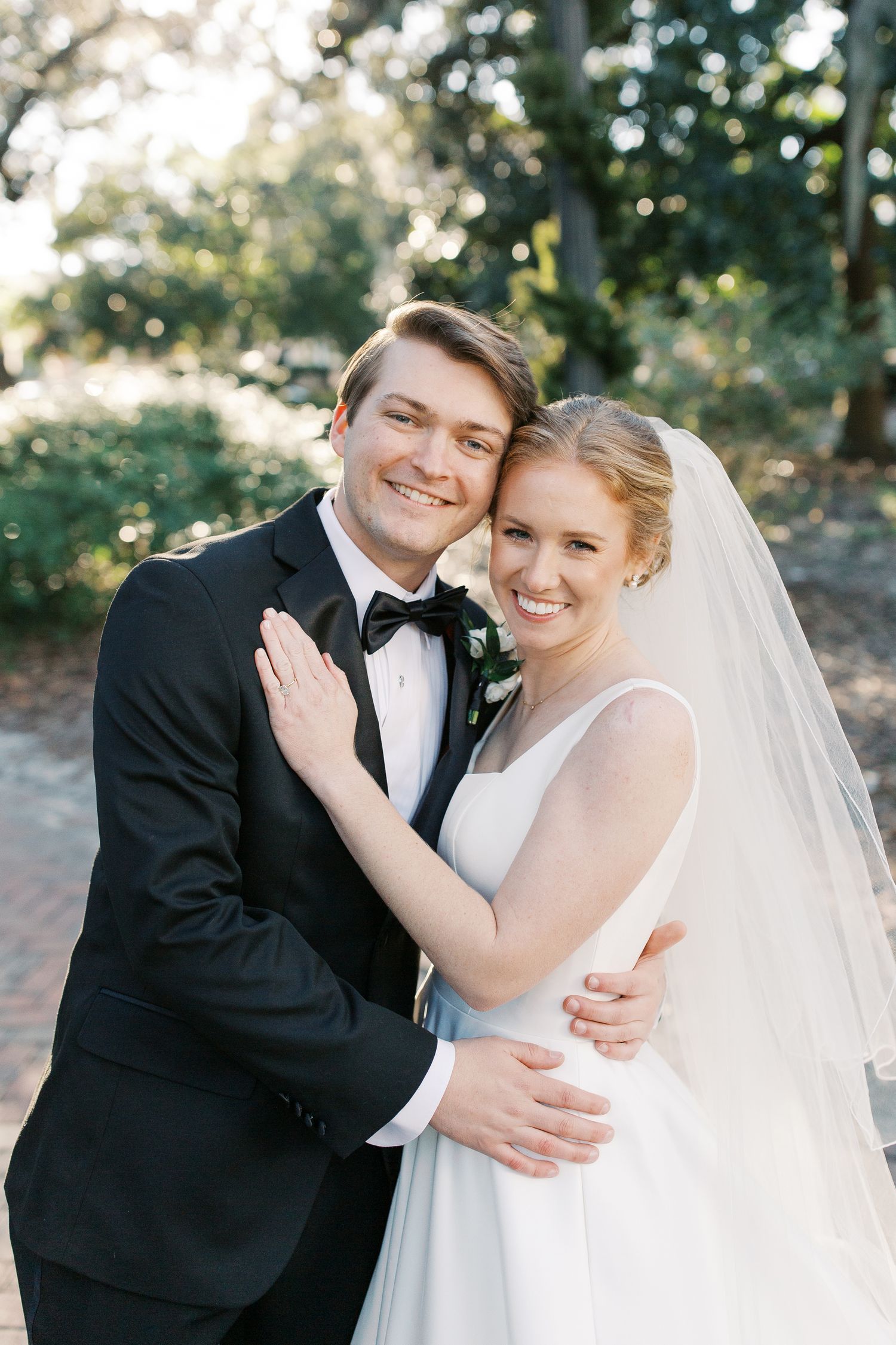 A romantic outdoor wedding portrait of a couple in formal attire with a dreamy bokeh background.