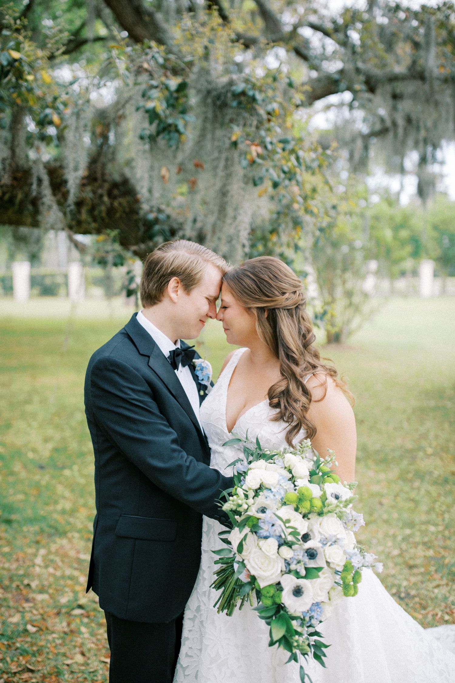 Intimate wedding portrait under moss-draped oak trees with lush white bouquet.