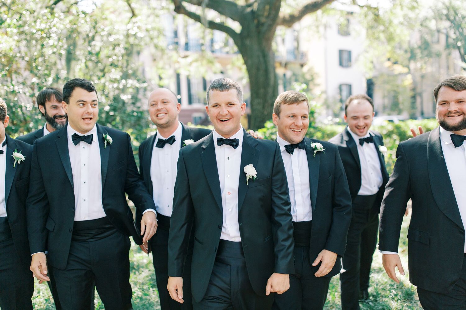 Groomsmen in black tuxedos walk together under oak trees in Monterey Square.