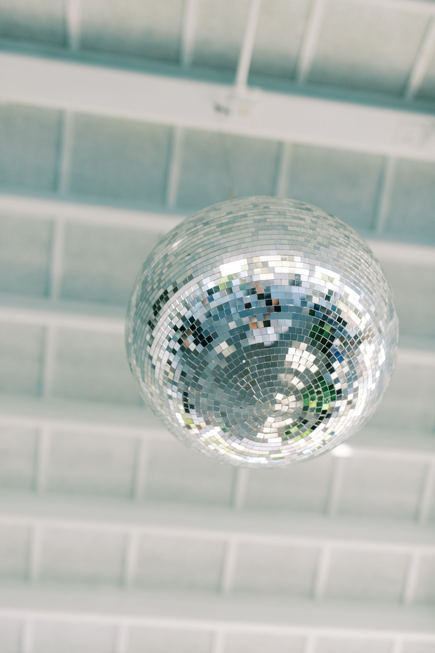 A shimmering disco ball hangs from a white ceiling, reflecting light in a classic retro party atmosphere.