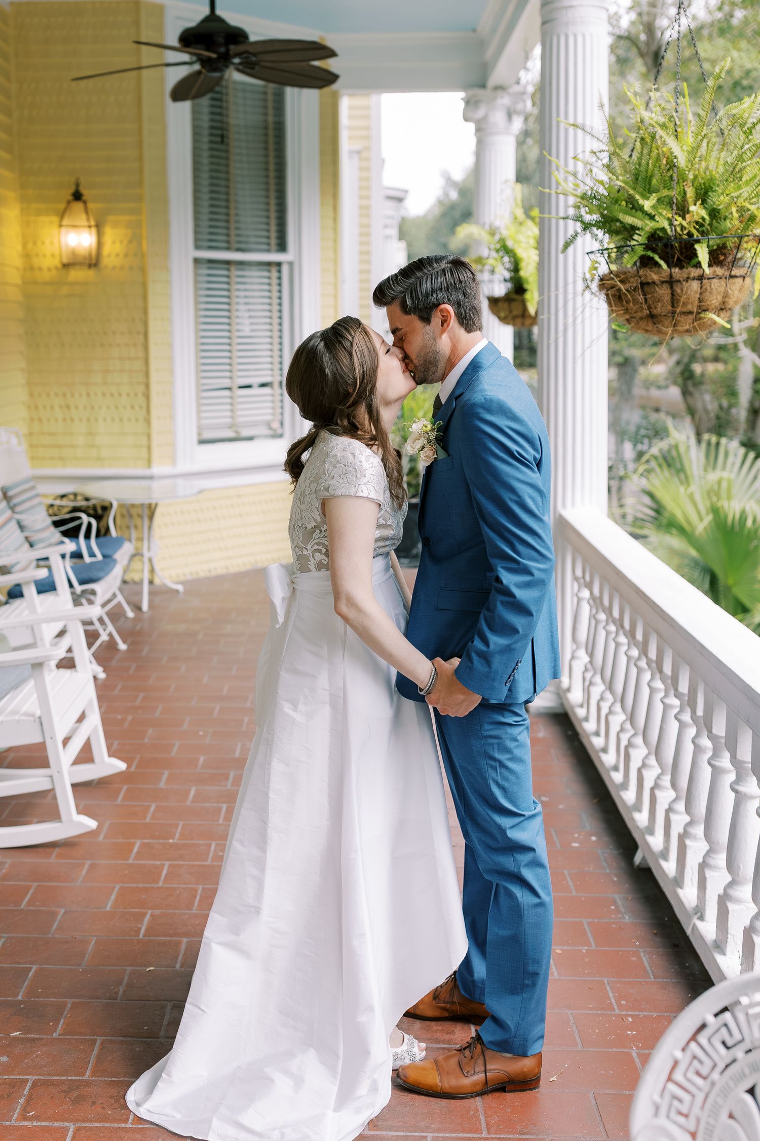 A romantic moment shared on a classic Southern veranda with white railings and ceiling fan.