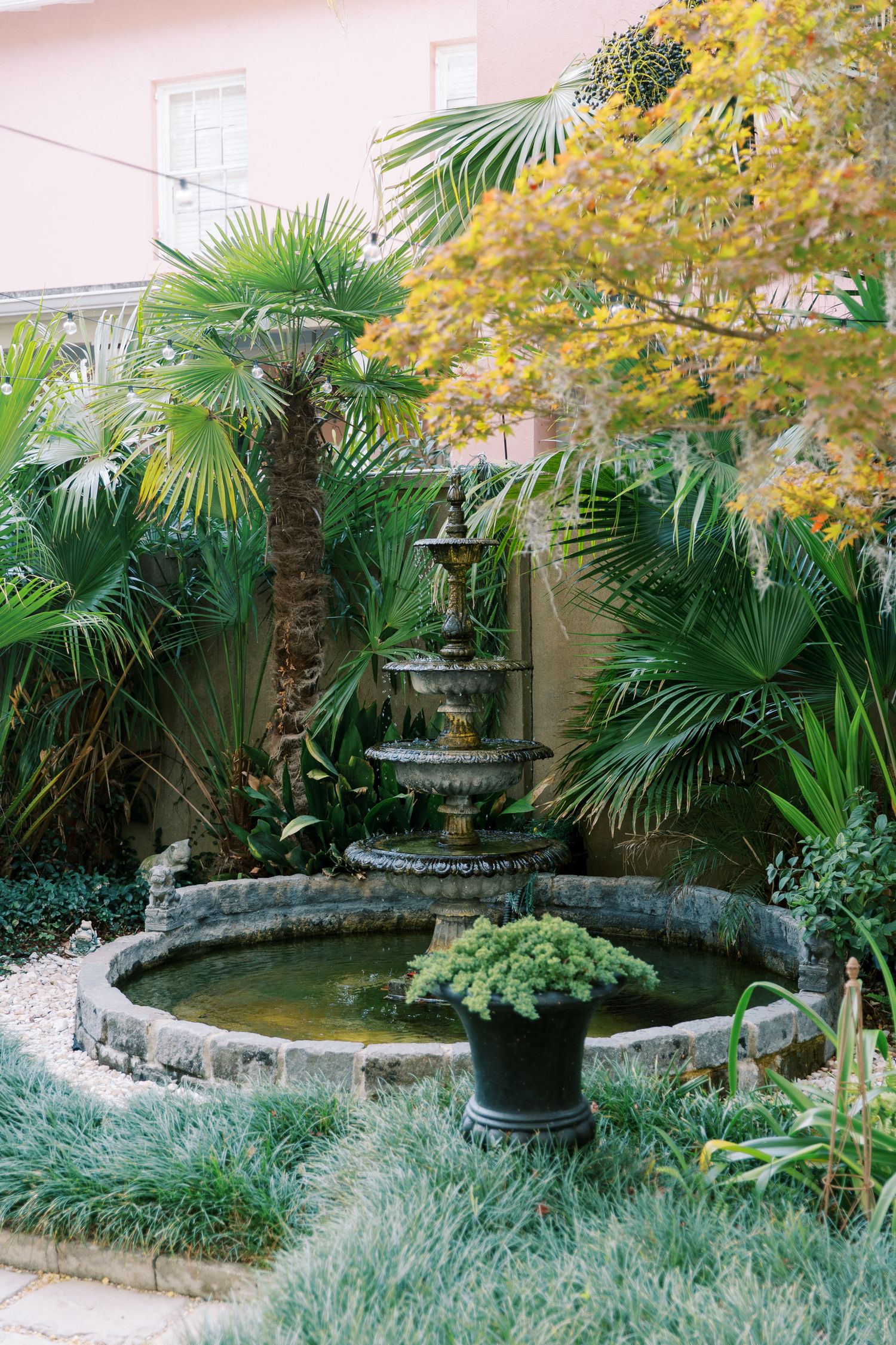A serene garden courtyard with palm trees, yellow foliage, and a stone water feature.