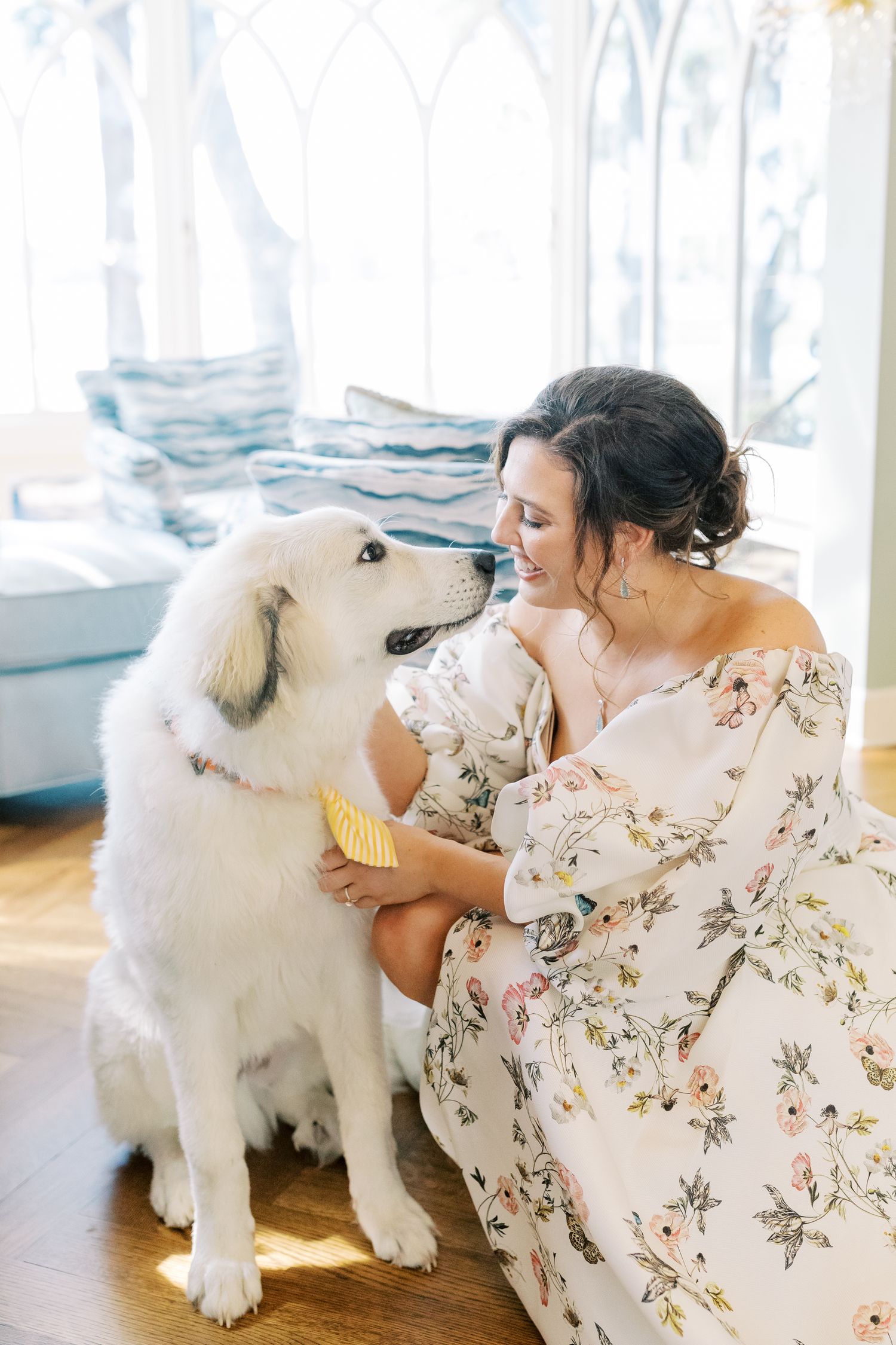 A large white fluffy dog shares a tender moment with someone in a floral dress by a window.