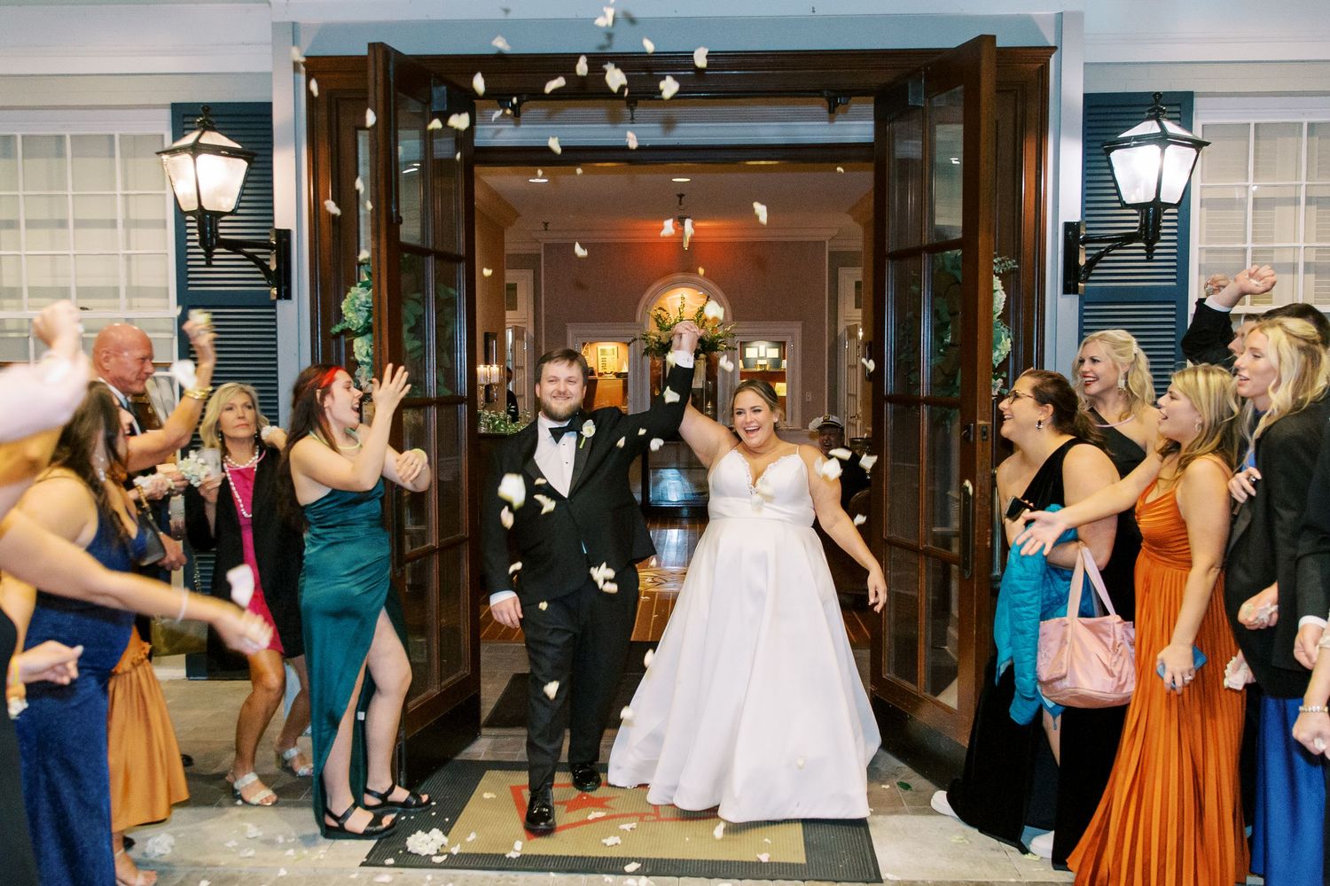 Wedding couple makes grand exit as guests toss confetti outside venue entrance.