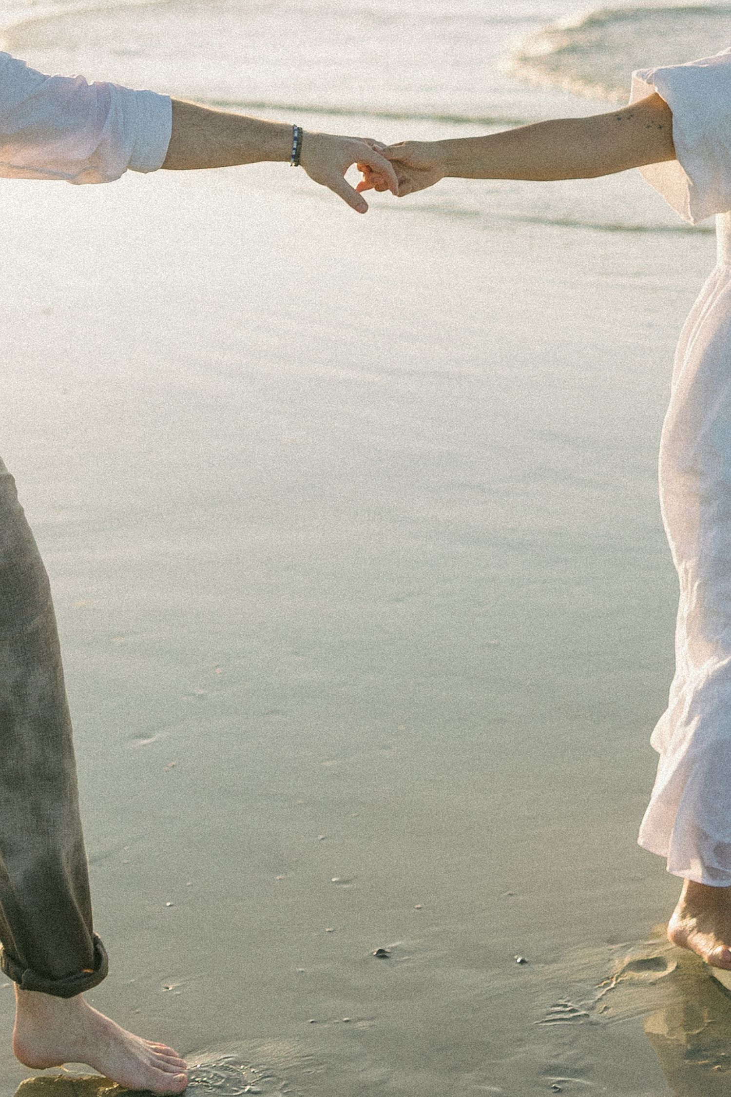 Barefoot couple walking together on a sandy beach during sunset.