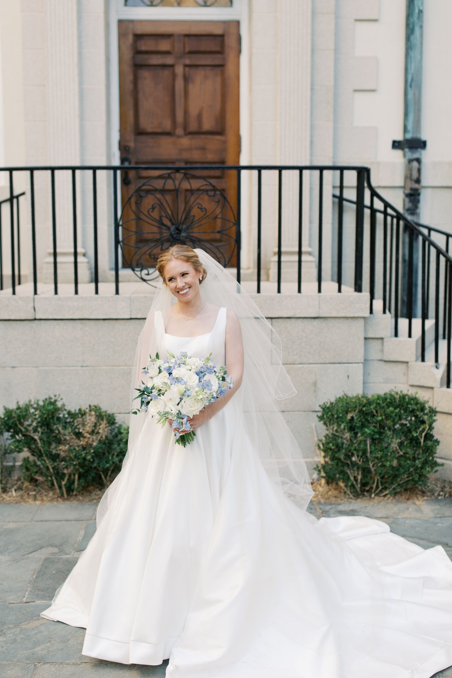 Classic wedding portrait showing elegant bride in flowing white gown and veil on church steps.