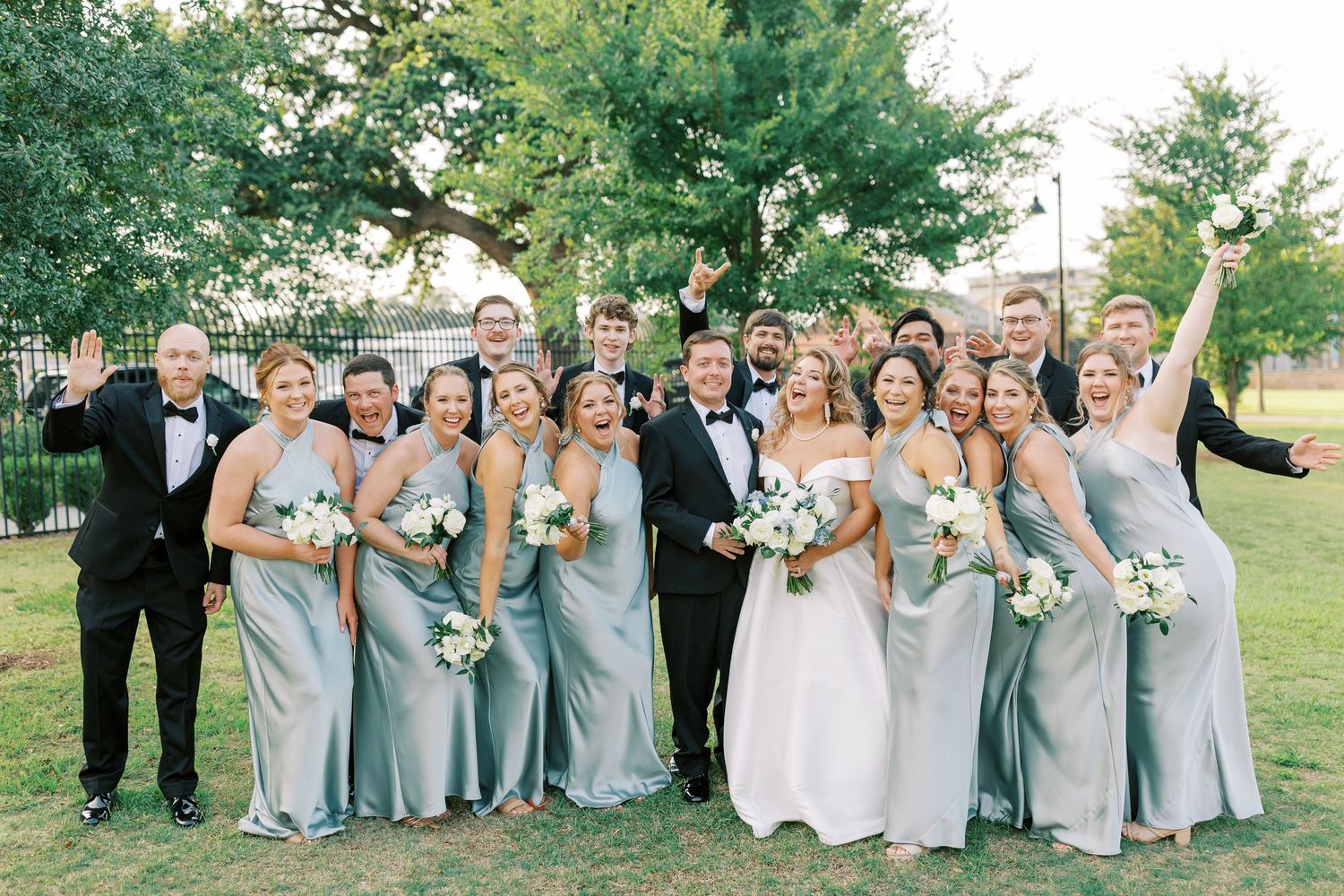 Wedding party in blue attire poses together on green lawn during summer celebration.