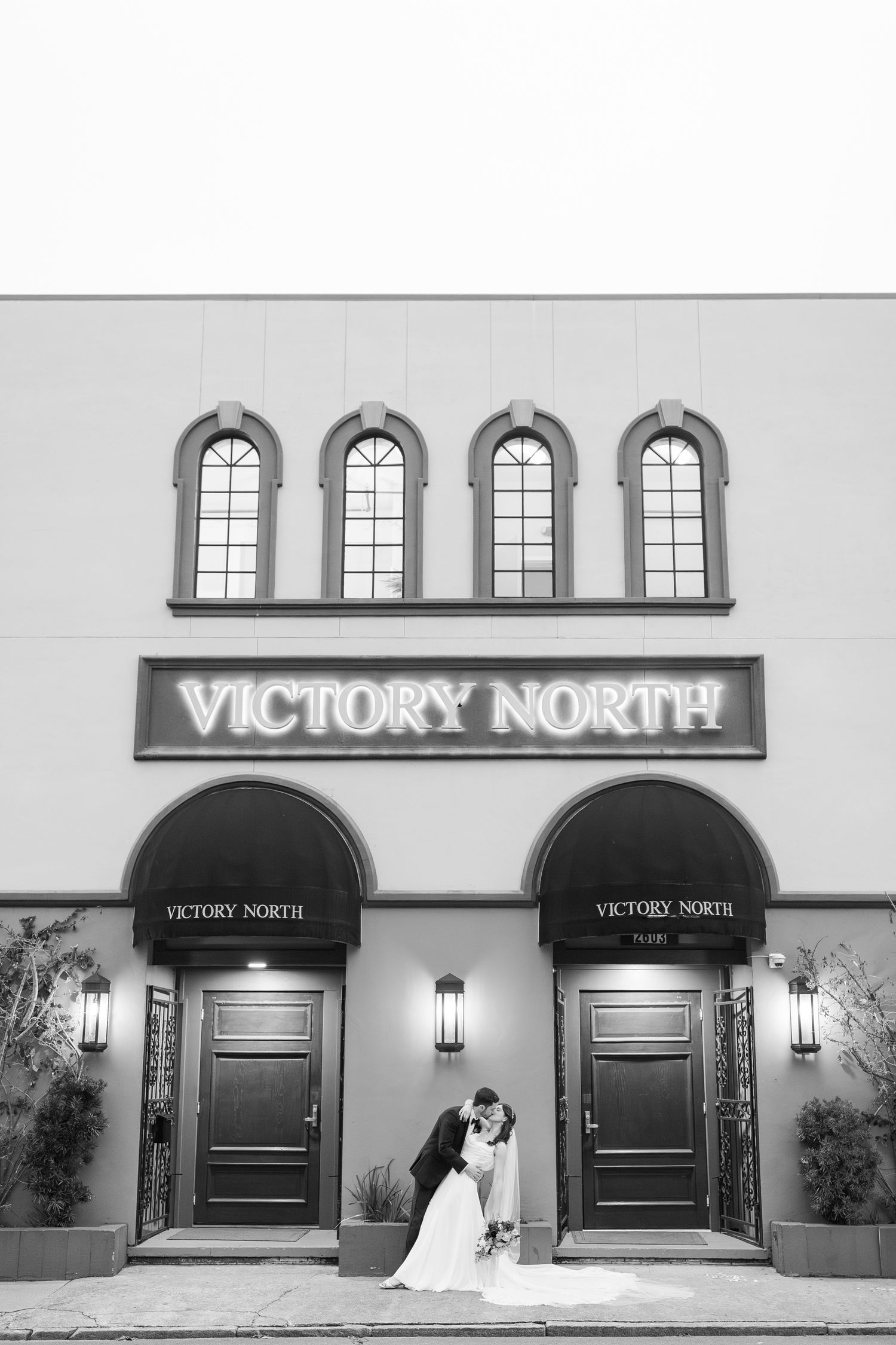 A romantic black and white photo of a couple at Victory North venue with arched windows above.
