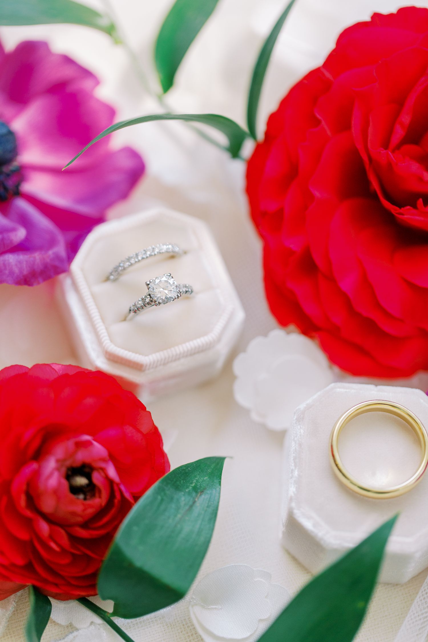 Diamond engagement rings in a white velvet box surrounded by red and pink flowers.