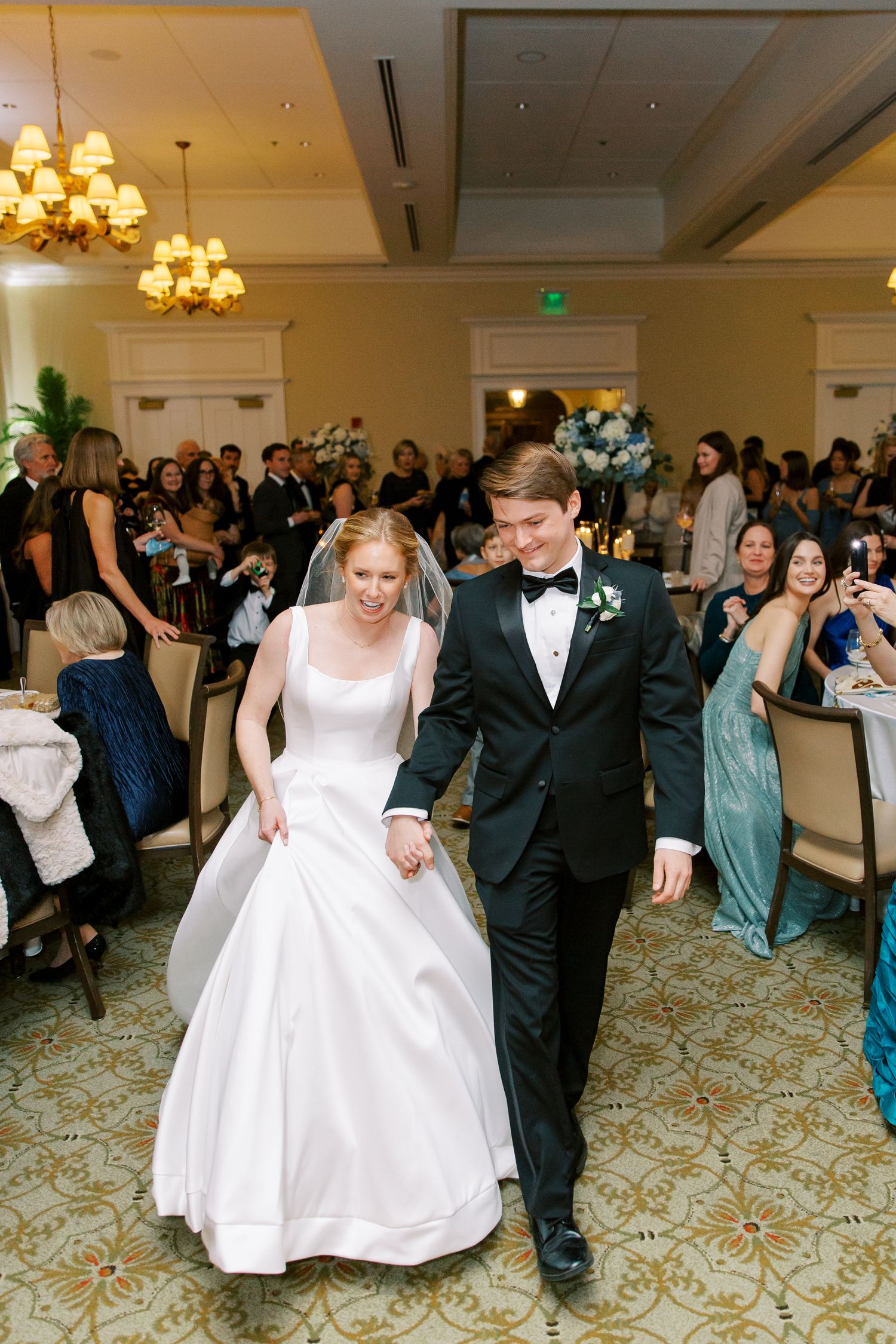 Wedding reception celebration in an elegant ballroom with ornate carpeting and chandeliers.