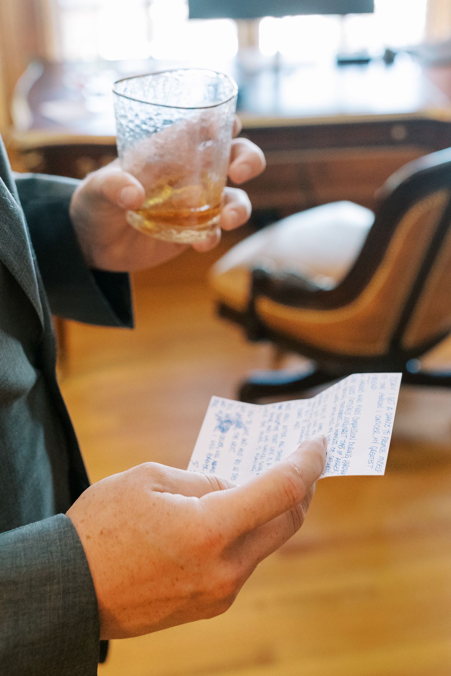 A person holds a beverage in a textured glass while looking at a handwritten note in an indoor setting.
