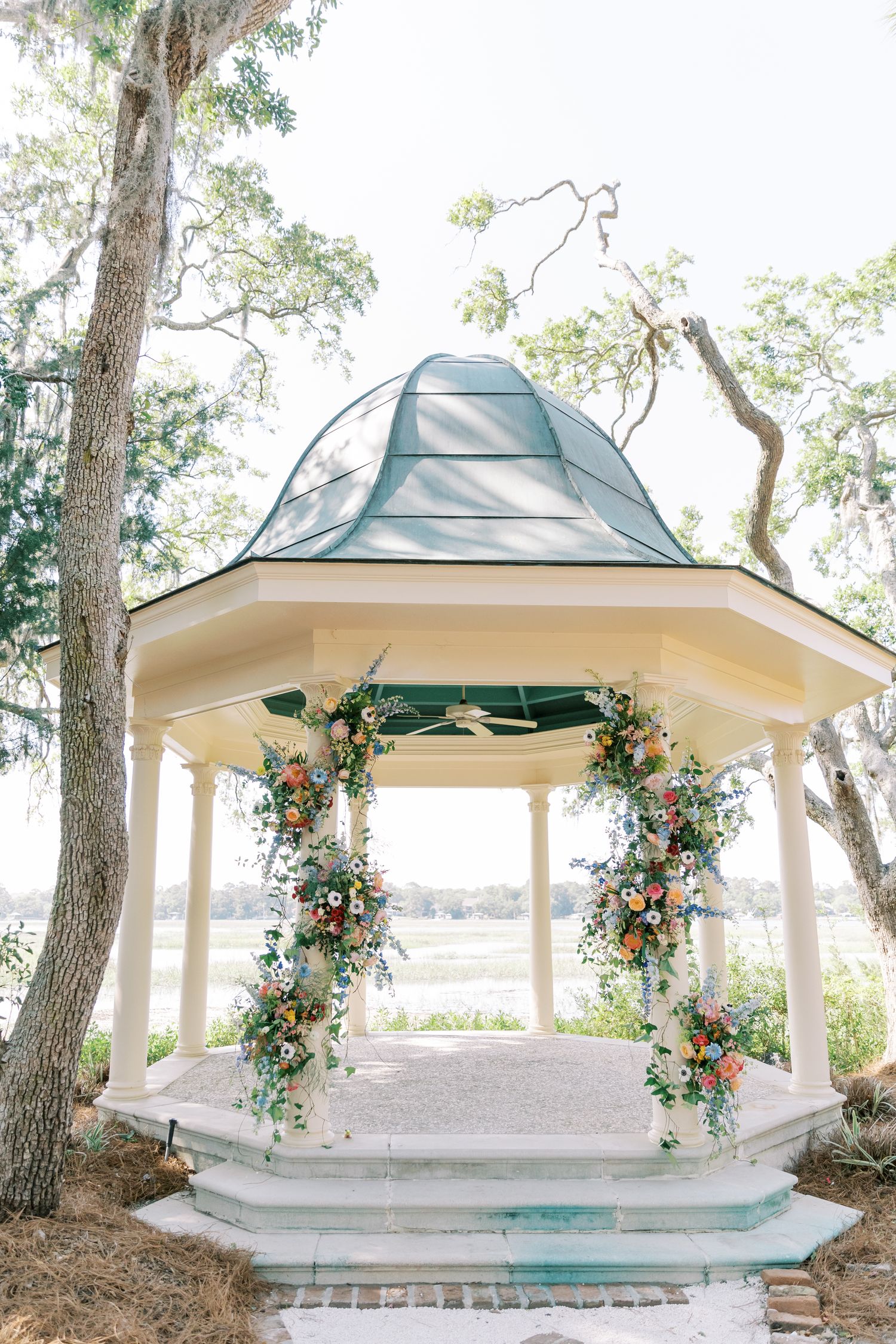 White gazebos decorated with floral arrangements stand elegantly among trees in an outdoor wedding venue.