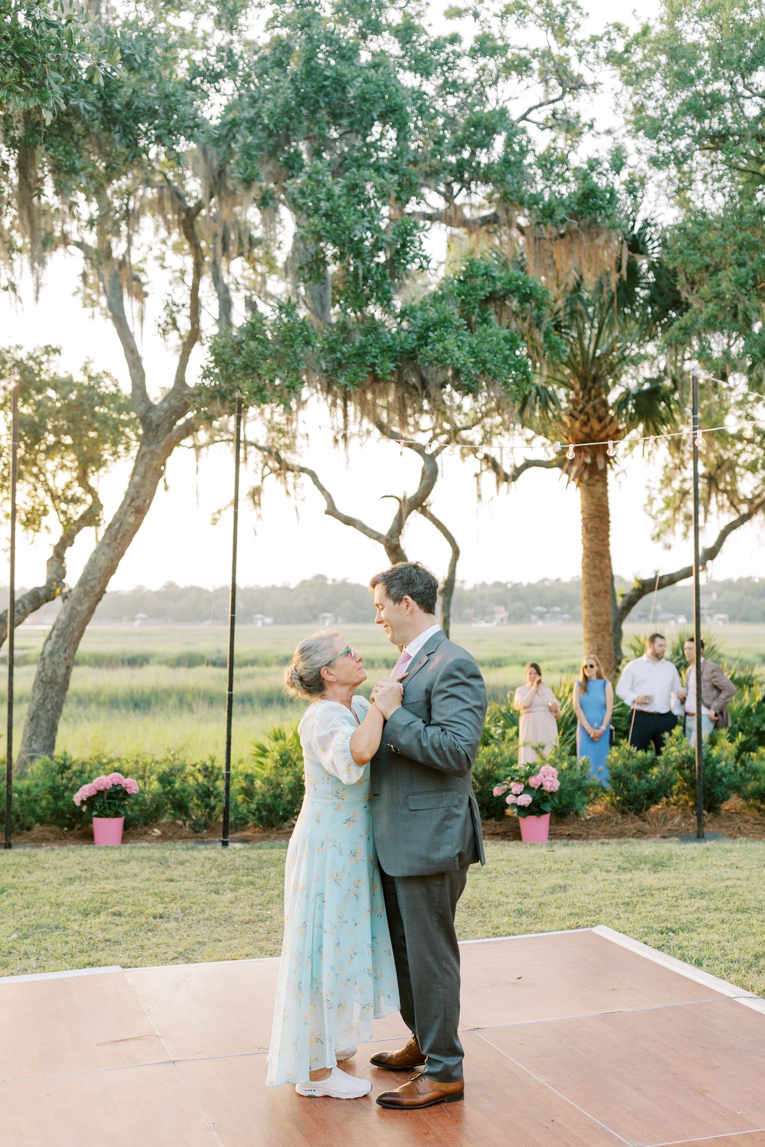 A couple dances on an outdoor patio under Spanish moss draped trees at sunset.