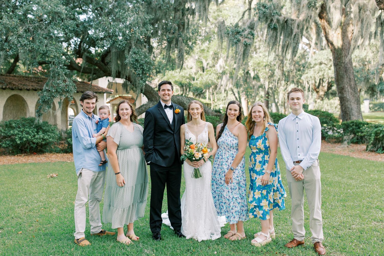 Wedding party poses together on a lush green lawn with Spanish moss draped trees in the background.