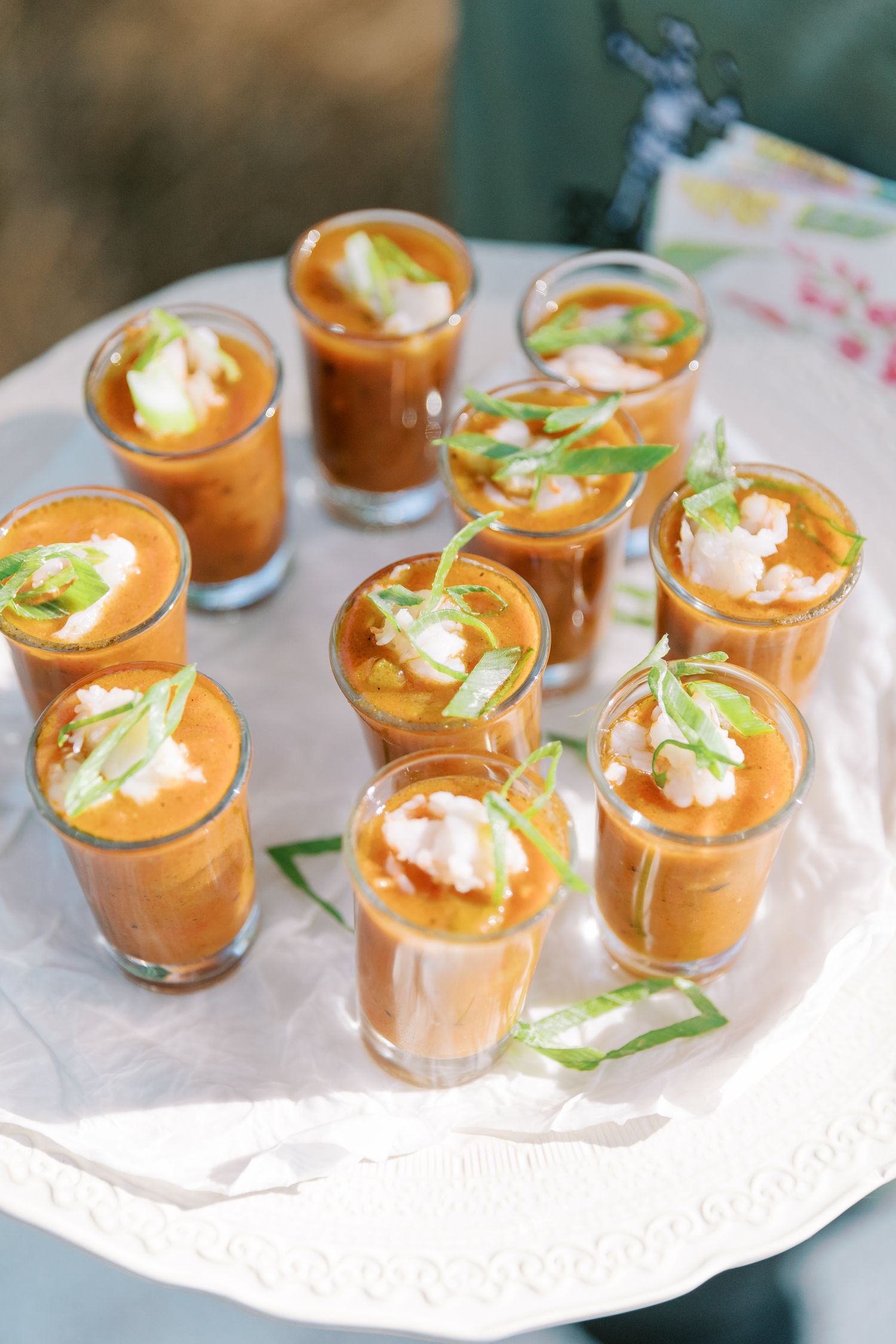 Small cups of orange-colored soup appetizers garnished with cream and herbs on a white serving platter.