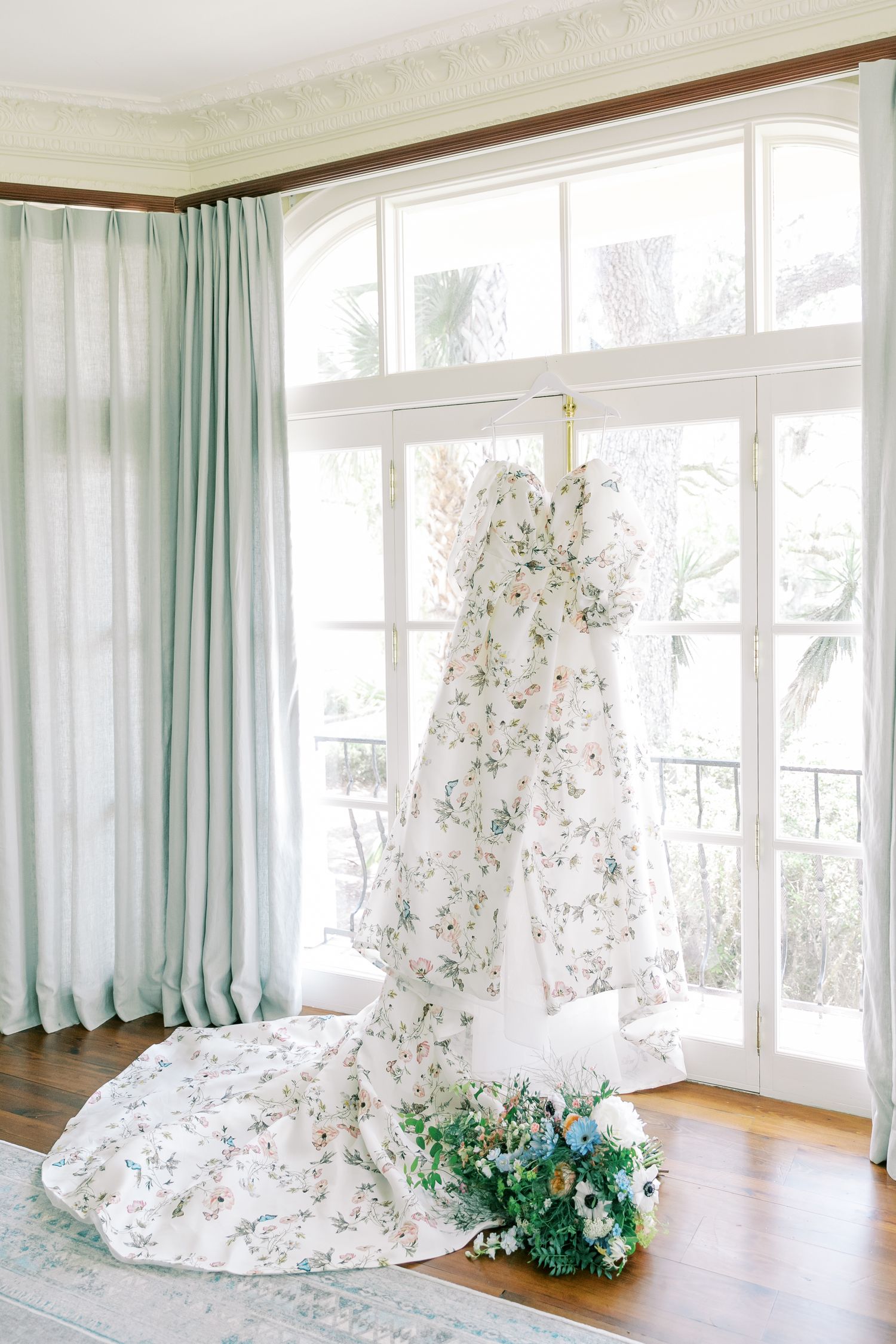 A bright sunlit room with large windows features a draped floral fabric and green decorative elements on the floor.