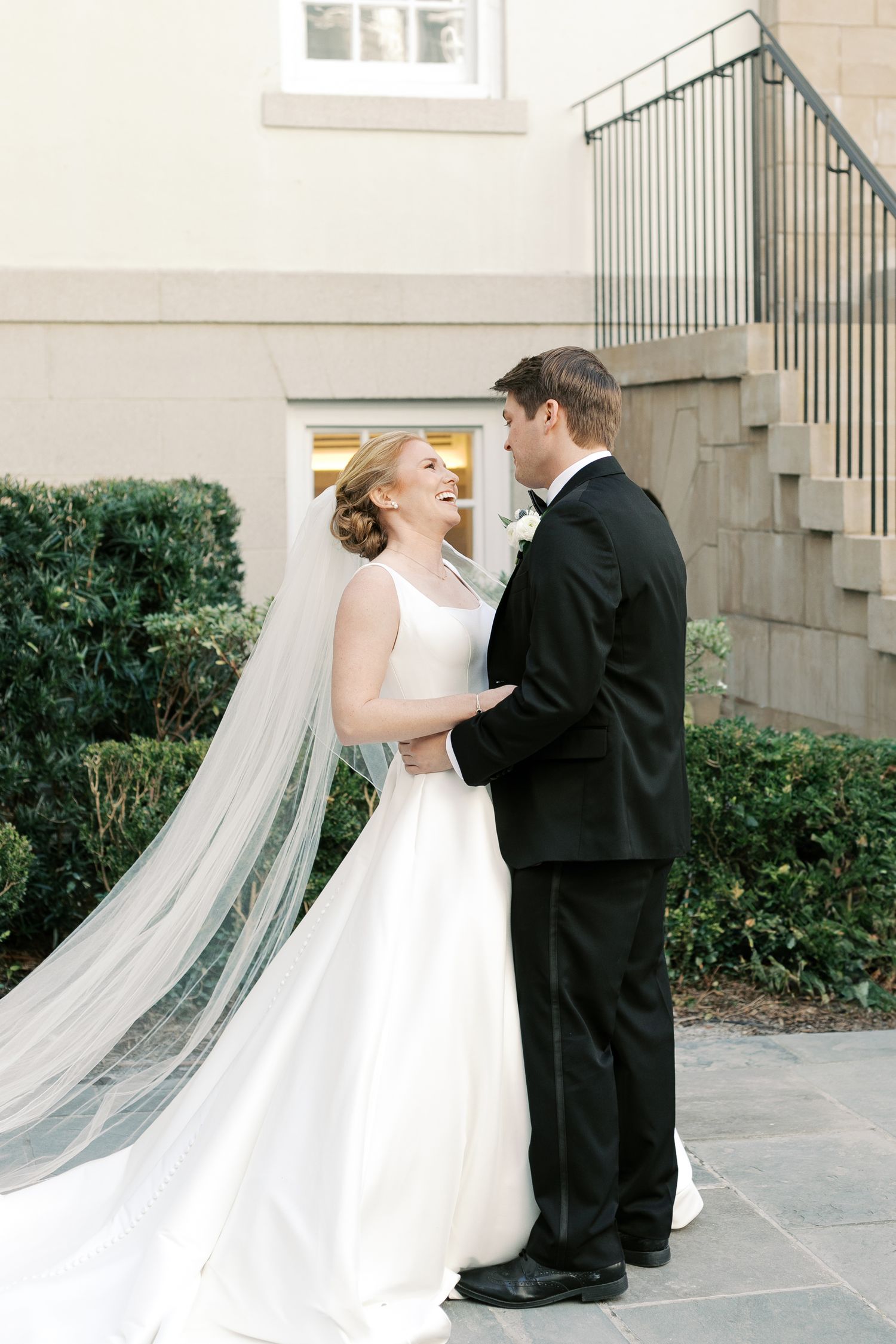A joyful wedding moment captured outdoors with the bride in a flowing white gown and long veil.