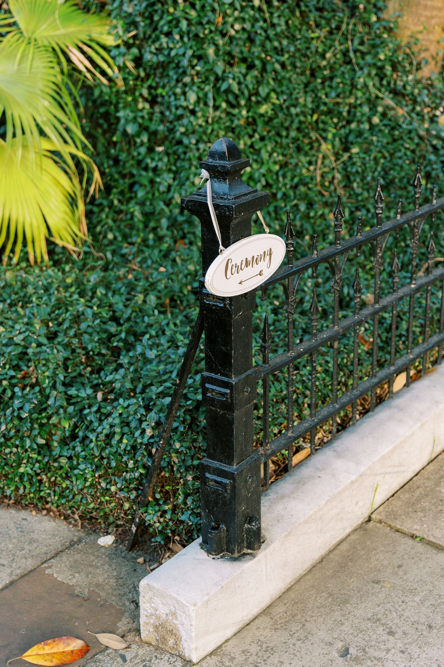Decorative black iron fence post with a ceremony sign against green foliage background.