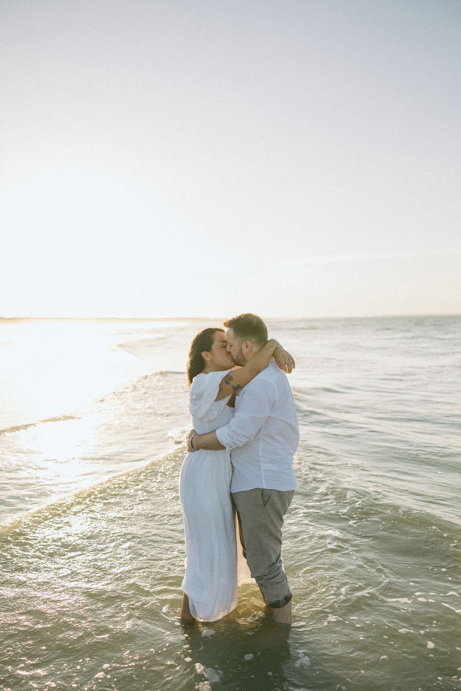 A couple embraces in the ocean waves during sunset creating a romantic silhouette against the horizon.