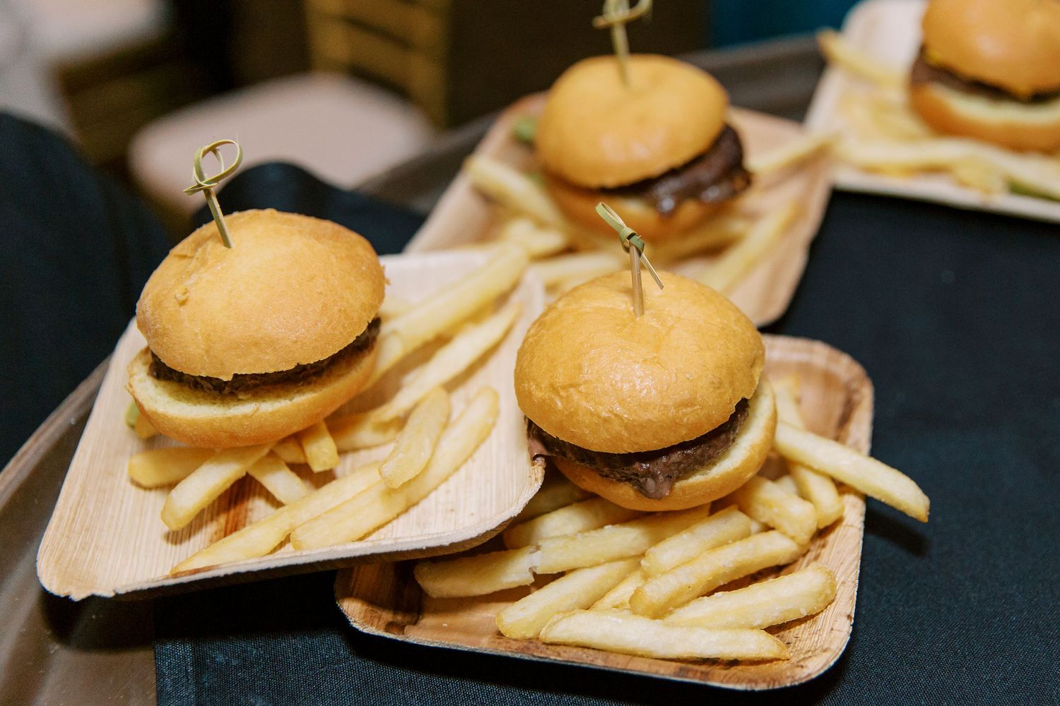 Three mini hamburgers with french fries served on wooden boards at wedding reception.