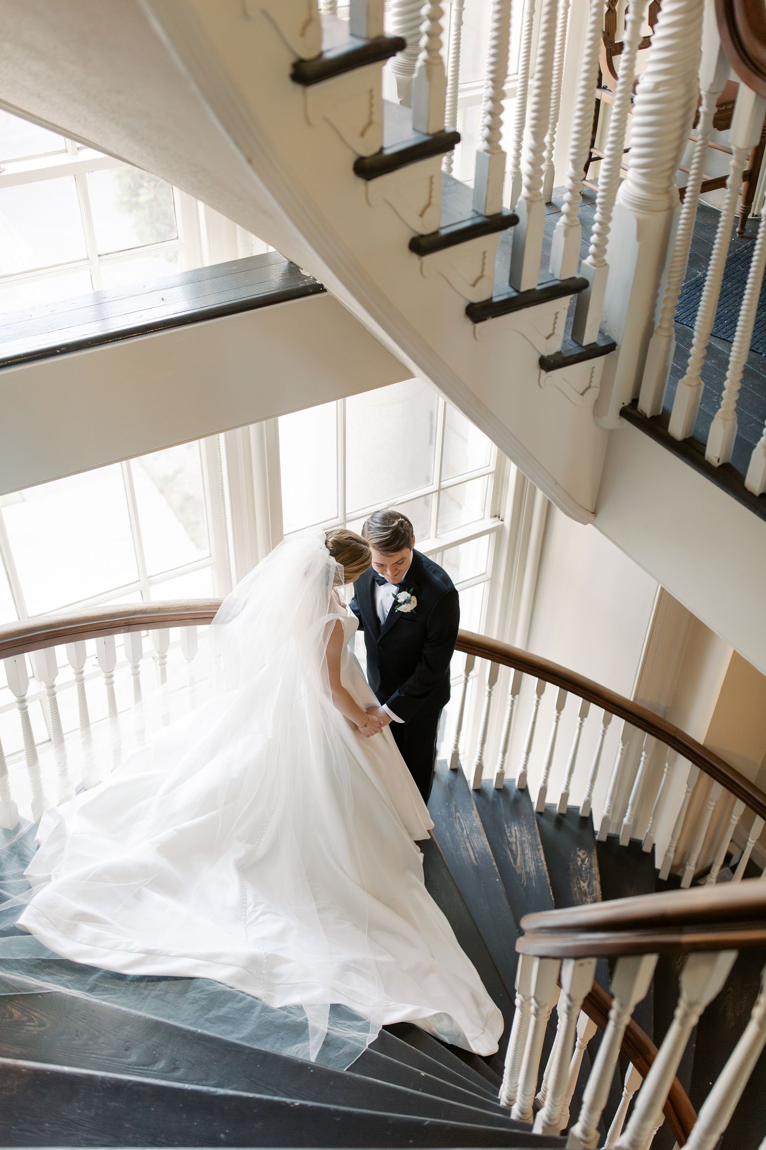 Wedding couple posing on an elegant spiral staircase with flowing dress train.