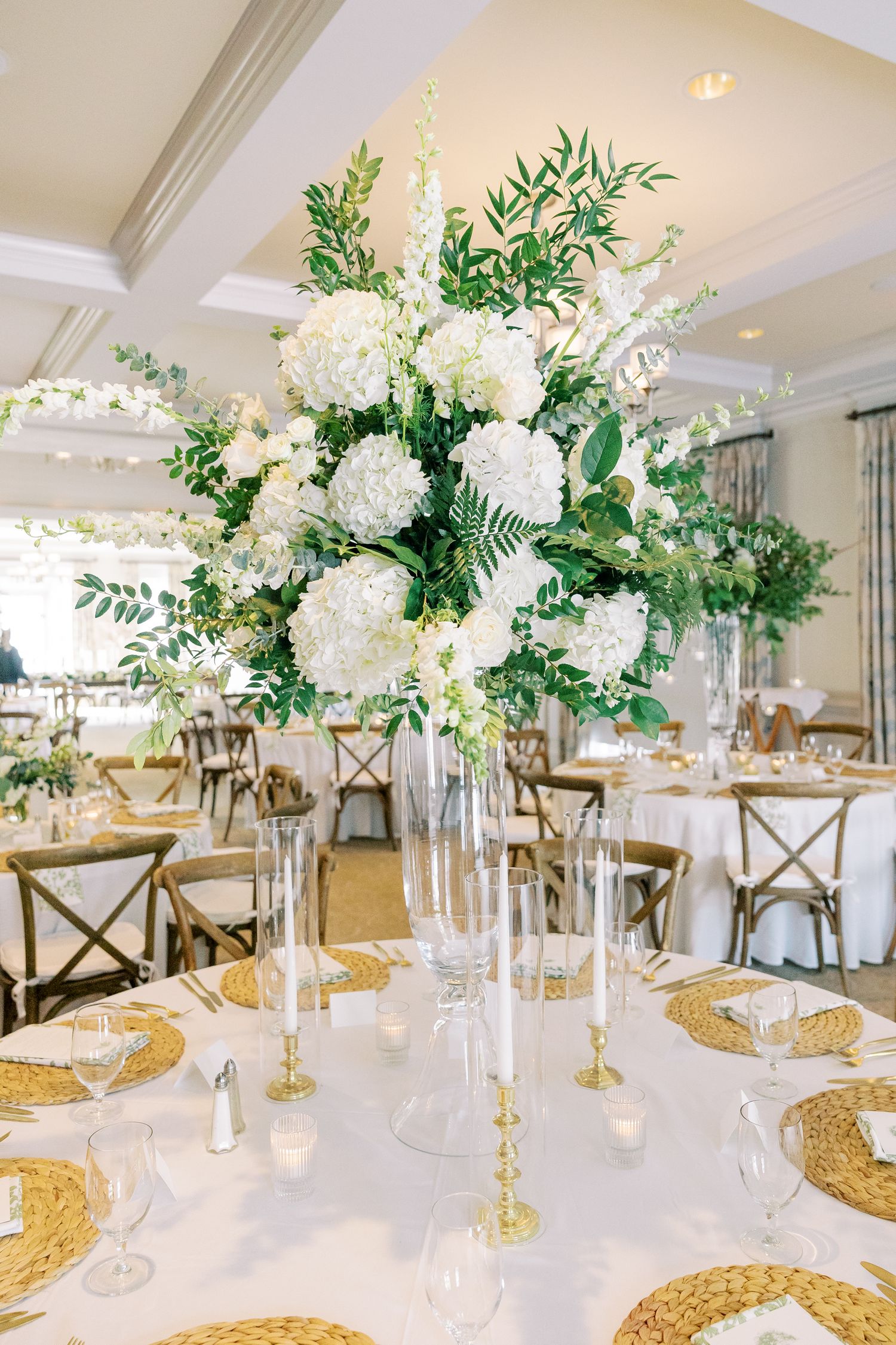 Elegant white and green floral centerpiece with hydrangeas on a table with gold charger plates at a wedding reception.