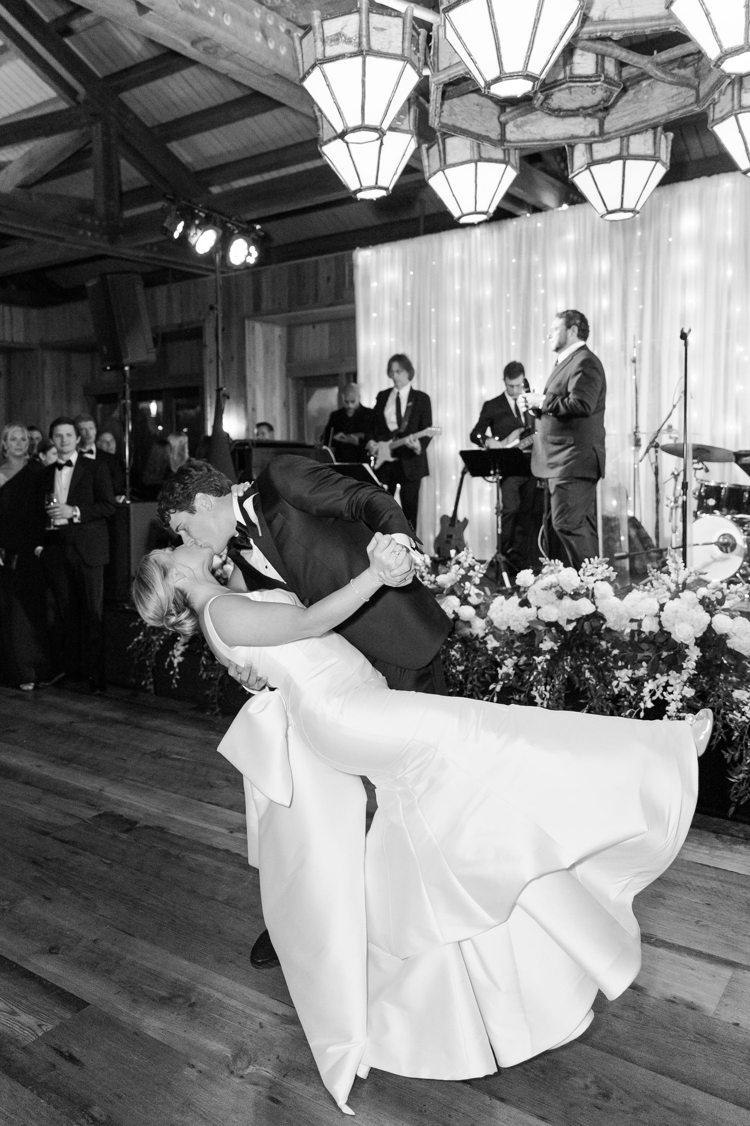 A dramatic black and white photo of a wedding dance with elegant lighting and floral decor.