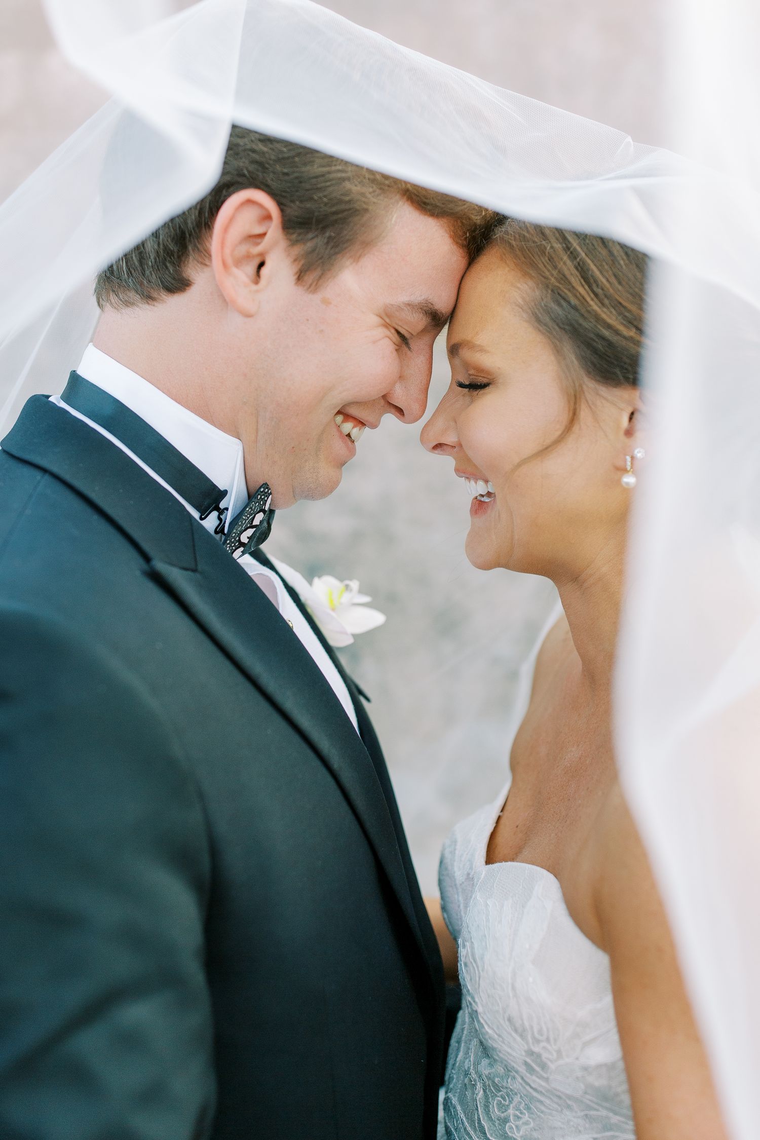 Intimate moment between wedding couple under flowing veil.