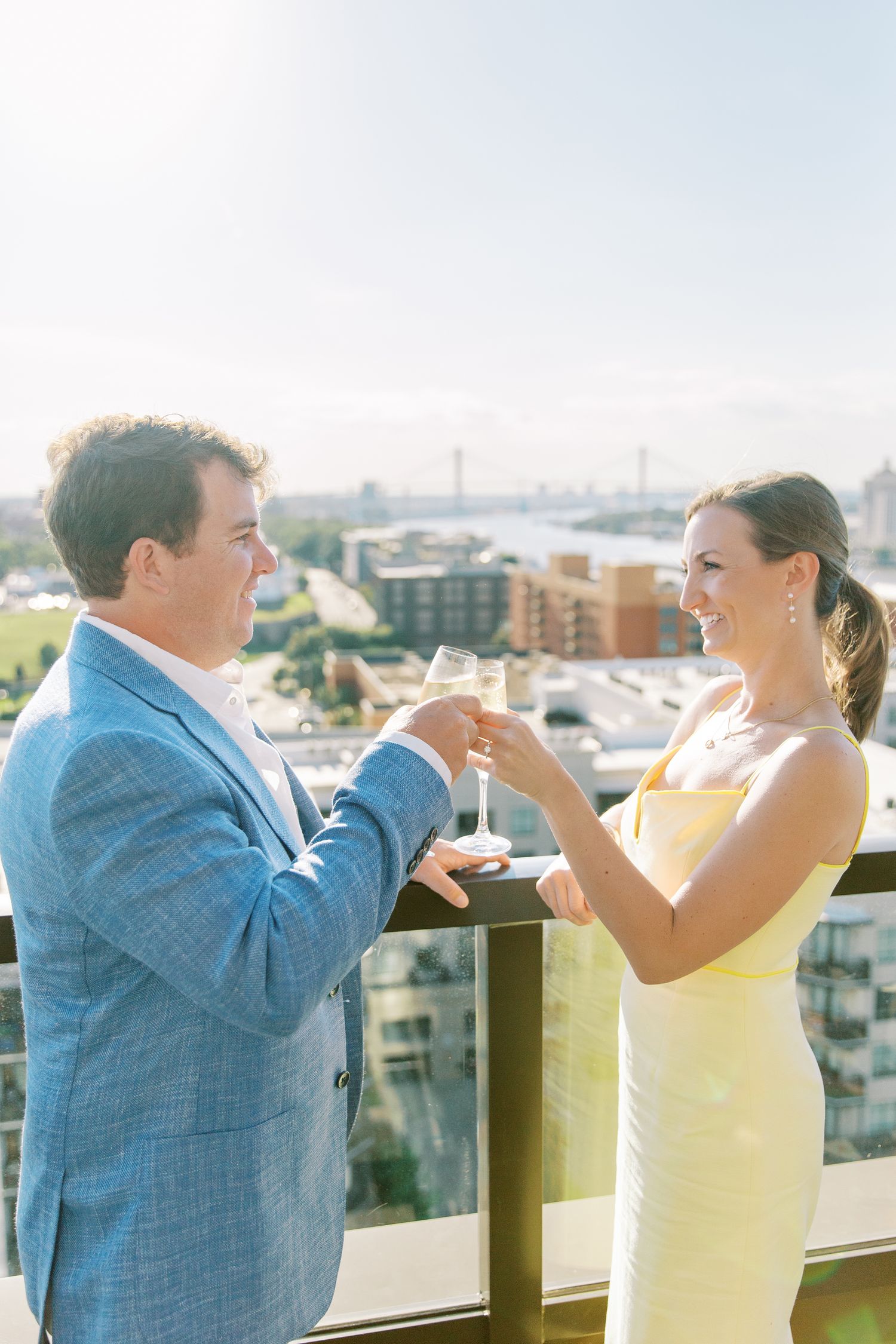Couple in formal attire toasts with champagne on rooftop balcony overlooking city skyline at The Thompson Hotel.