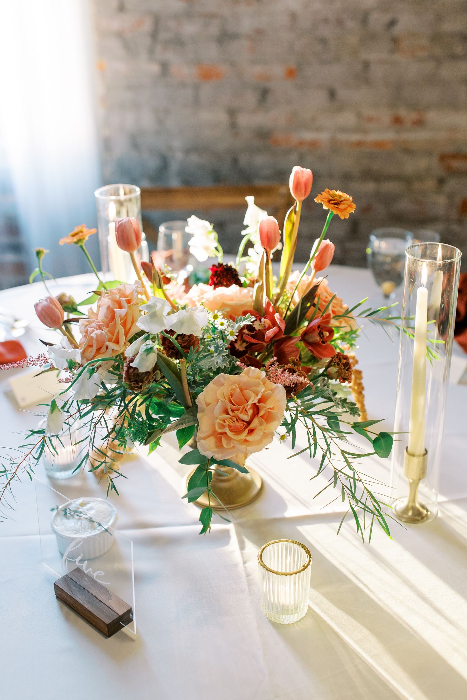 Elegant peach and coral centerpiece with tulips and roses on white tablecloth with candlelight at the Bottleworks Building in Savannah, GA.