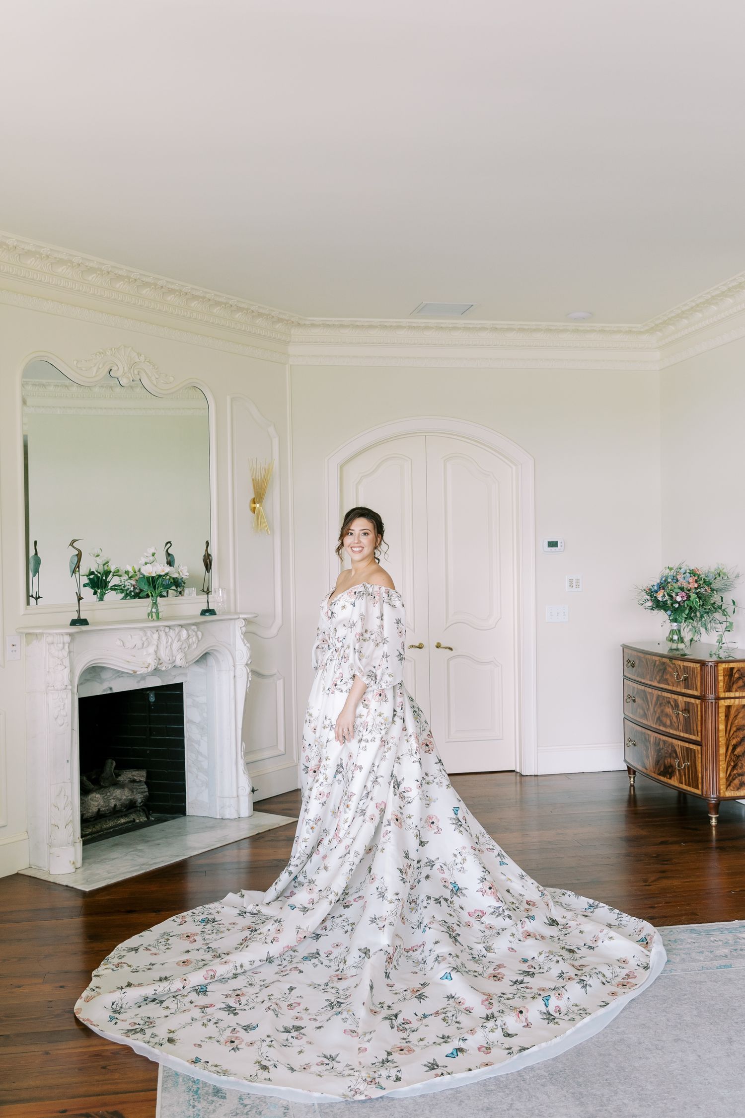 A stunning floral wedding dress with cathedral train photographed in an elegant white room with fireplace.