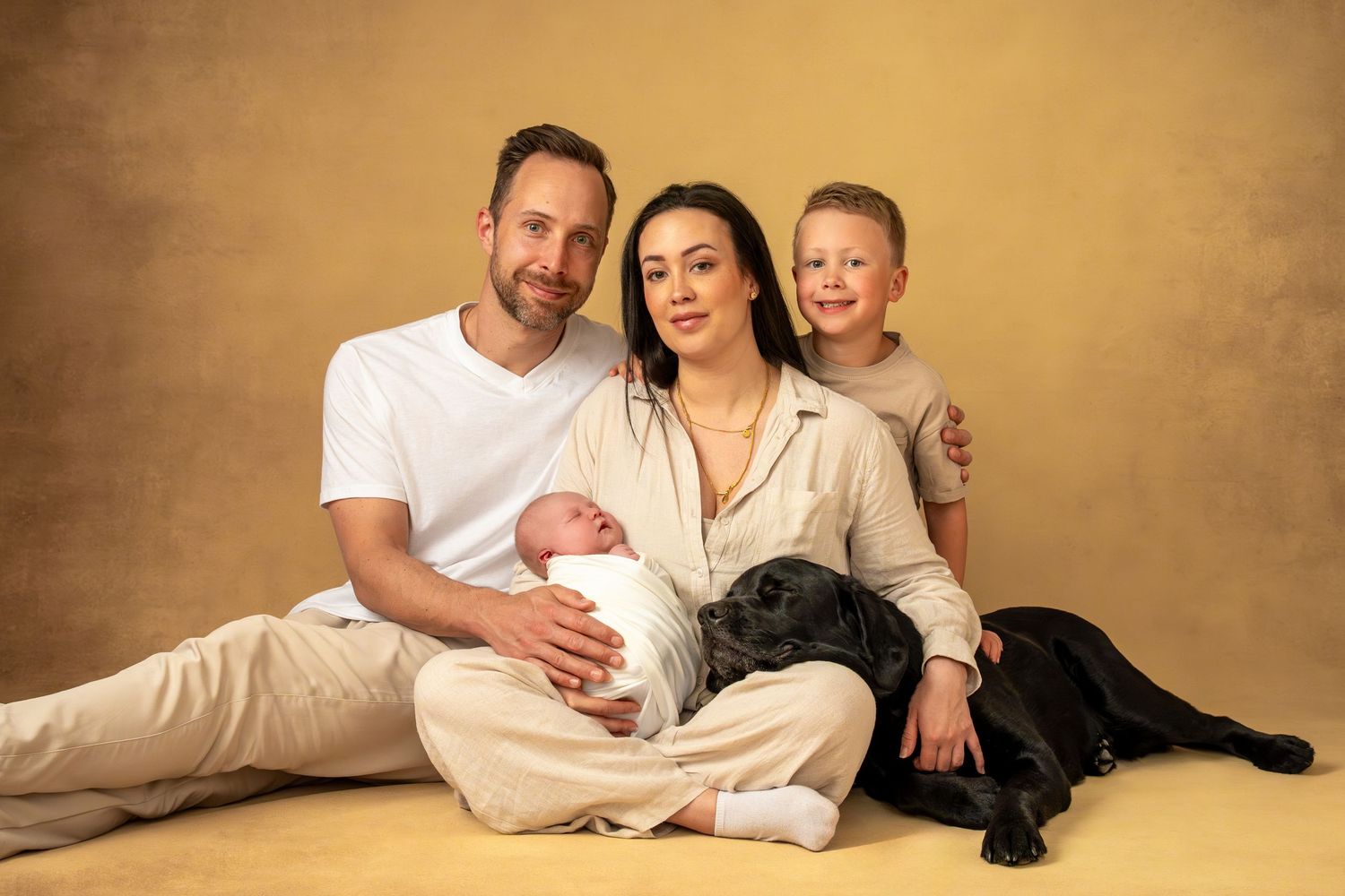 Familj med mamma, pappa, barn, bebis och hund sitter tätt tillsammans på golvet – tidlösa porträtt i Göteborg.