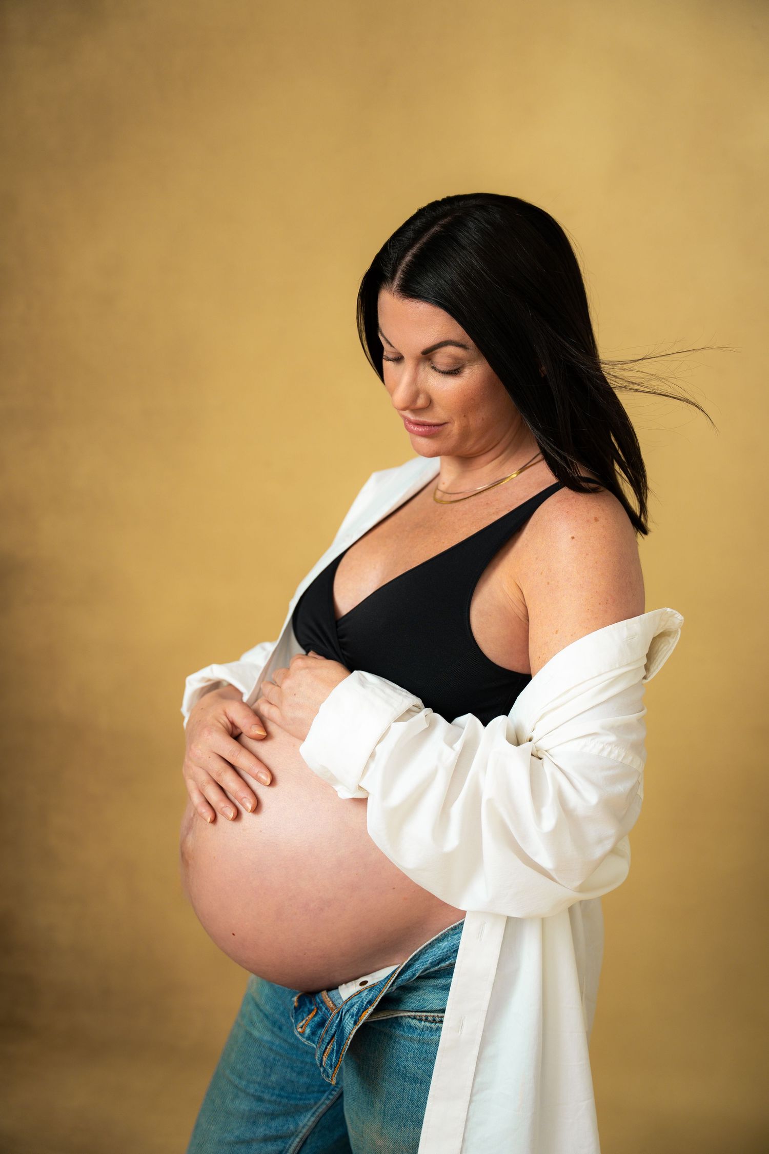 Gravidfotografering i studio – mamma håller händerna på magen med varm blick.
