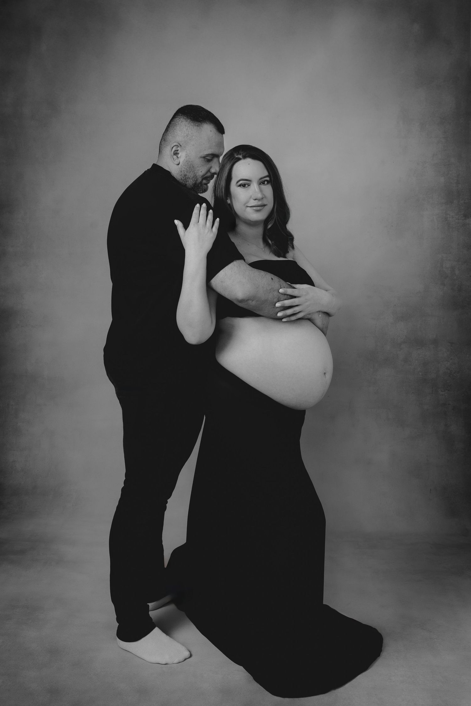 Gravidfoto med partner – par håller om magen under fotografering i studio i Jonsereds Fabriker Göteborg.