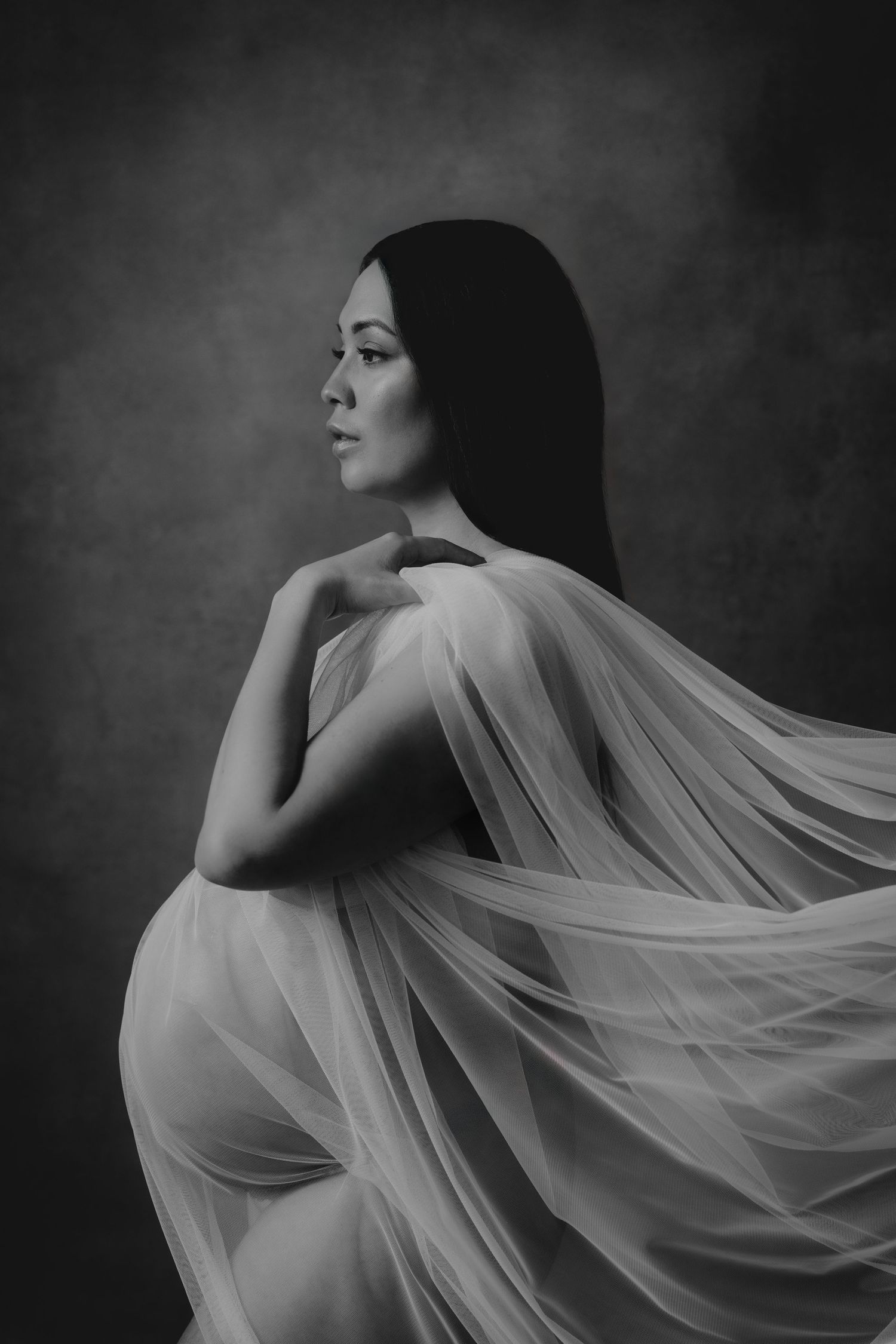 Studiofotografering gravid – elegant svartvitt porträtt av blivande mamma med tyg runt sig i Jonsereds Fabriker.