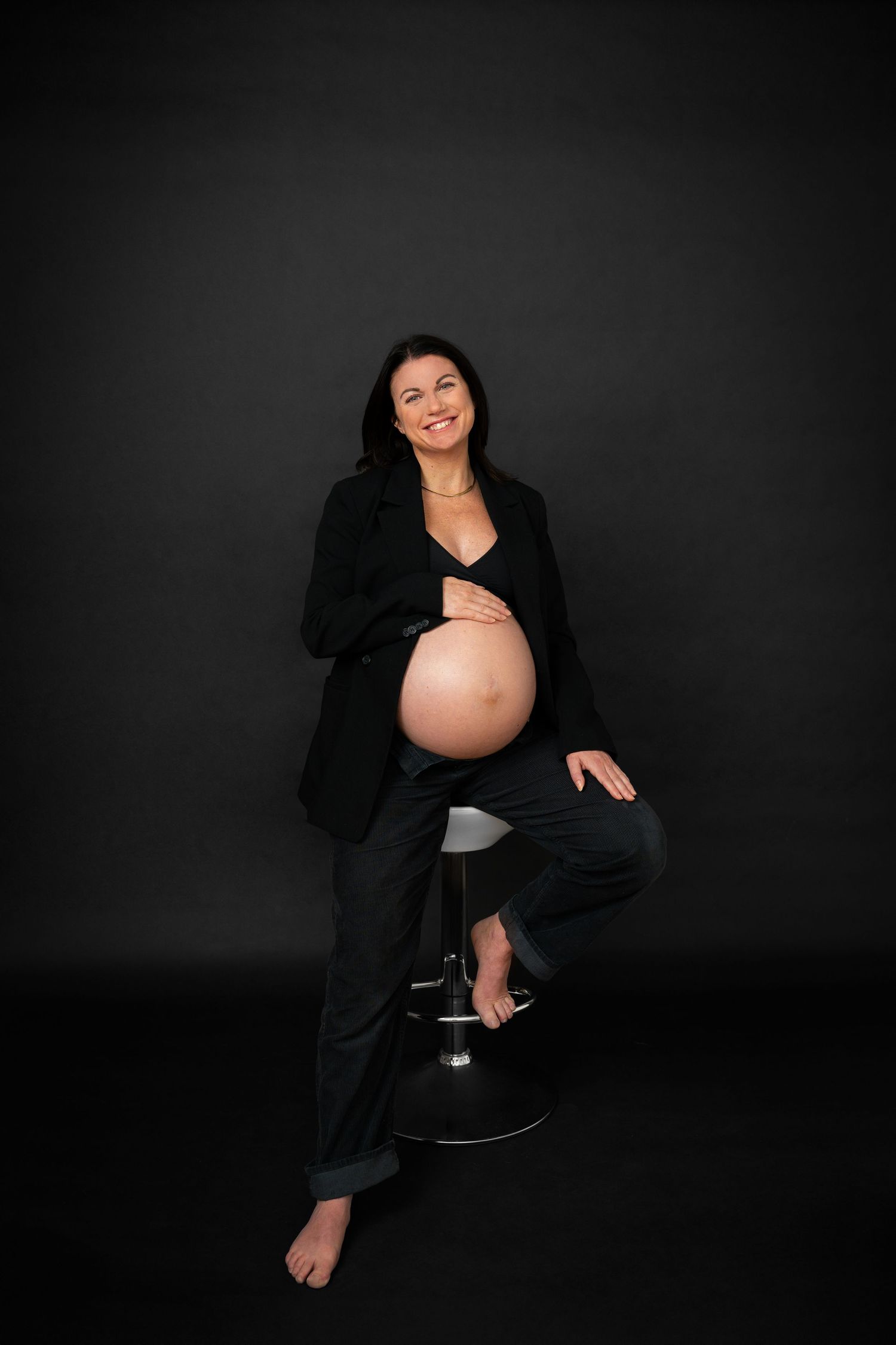 Gravidfotograf i Jonsered – stilfullt porträtt av blivande mamma med svart kavaj sittande på stol.