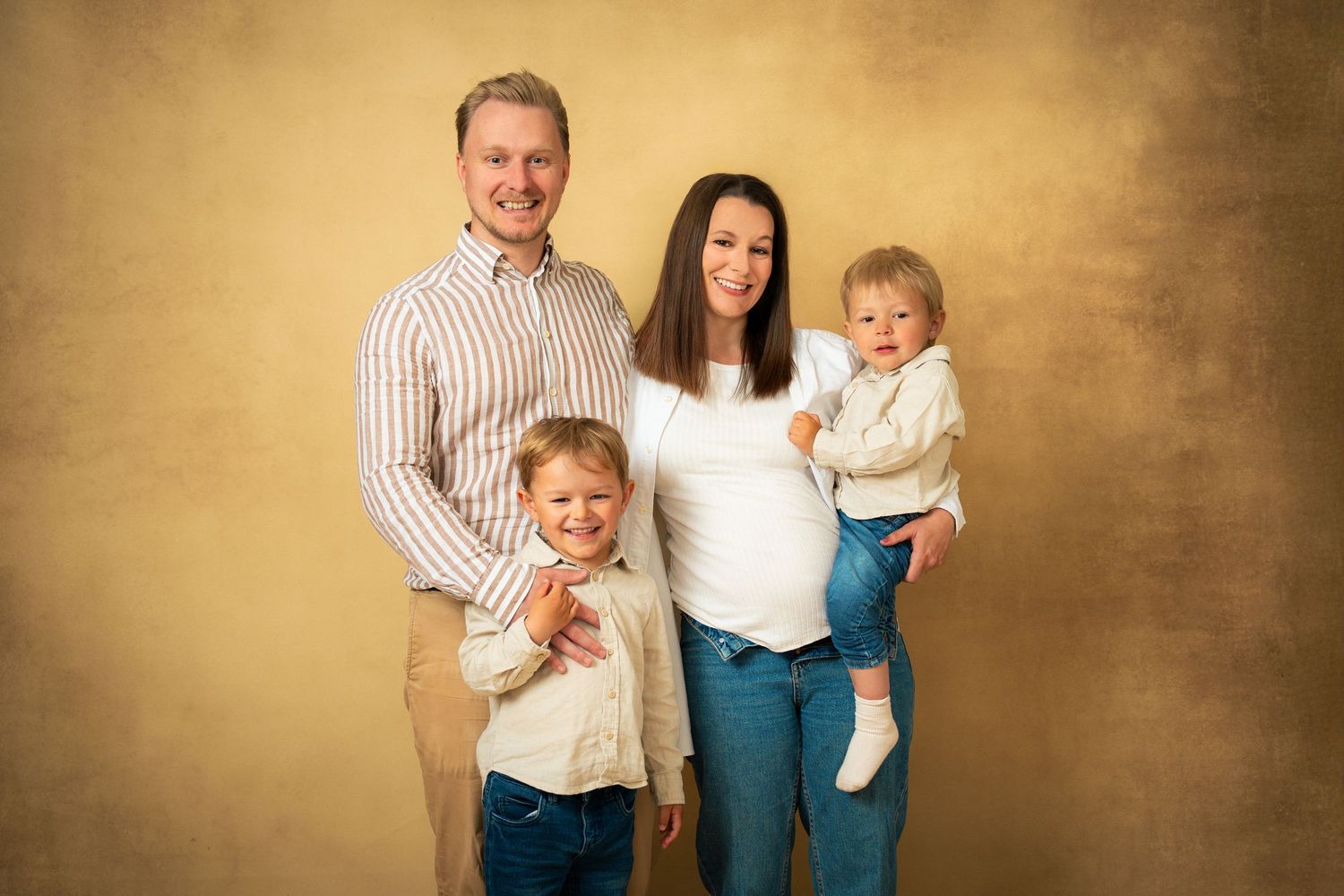 Familjebild i neutrala färger i studio i Göteborg – ett barn blir buren av mamma och ett barn står framför pappa.