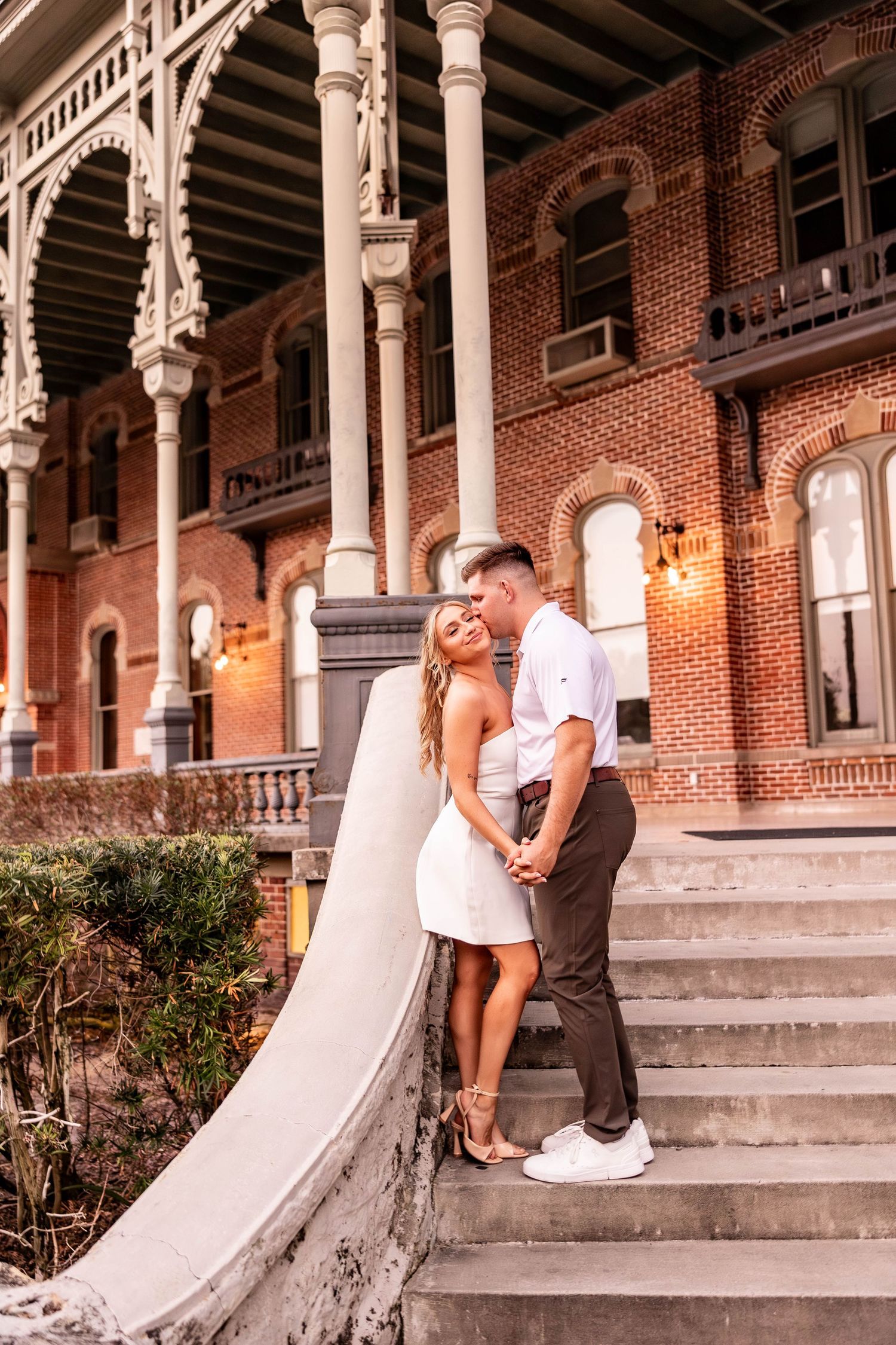Couple sharing a romantic moment on stone steps of a historic brick building with ornate columns.