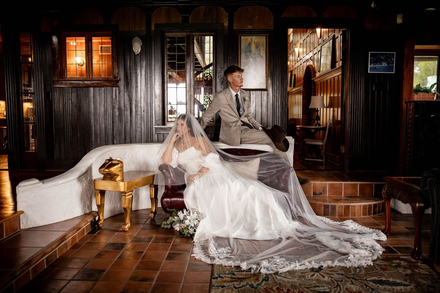 A bride in a flowing white wedding gown poses dramatically in a rustic barn setting with warm lighting.