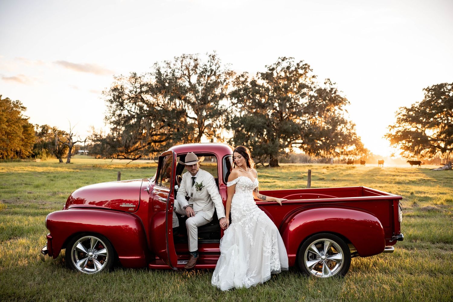 A romantic sunset photoshoot featuring a vintage burgundy car in a golden field at dusk.