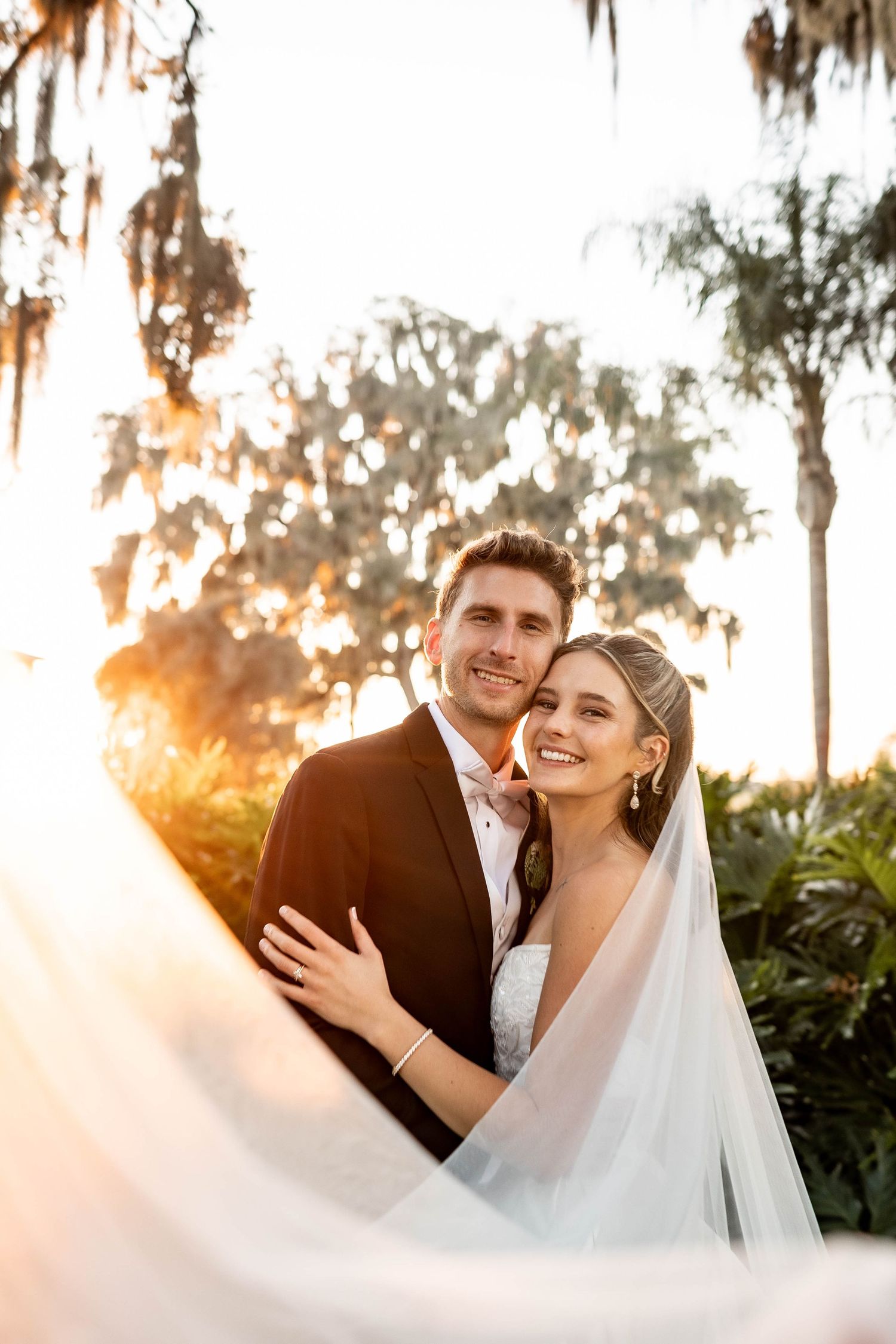 A romantic wedding couple embraces during golden hour sunset with Spanish moss draped trees in the background.