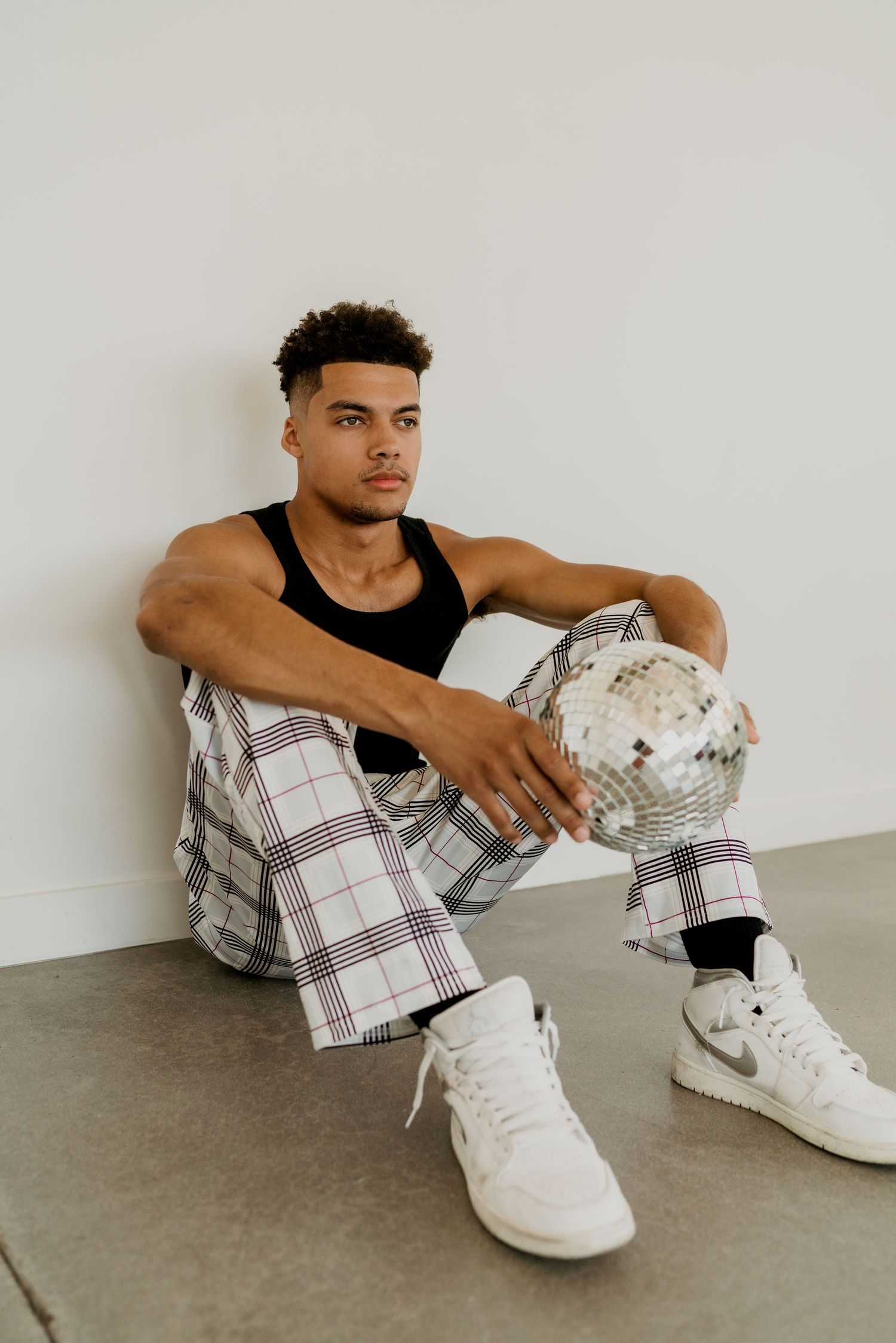 Young man in plaid pants sitting on floor holding a disco ball.