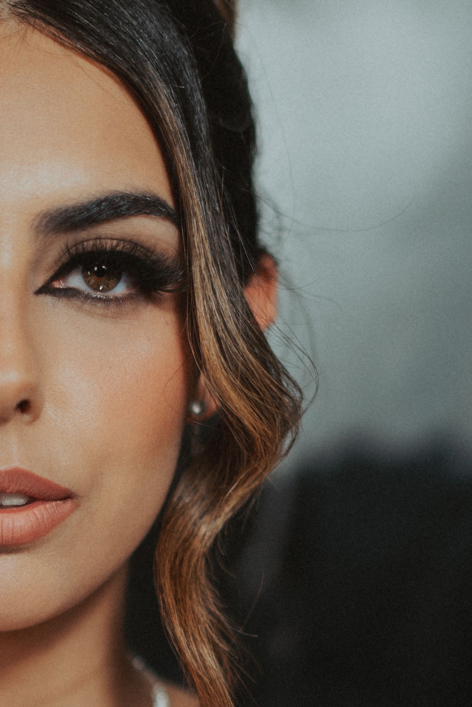 Close-up portrait of a woman with dramatic eye makeup, winged eyeliner, and highlighted brunette hair.