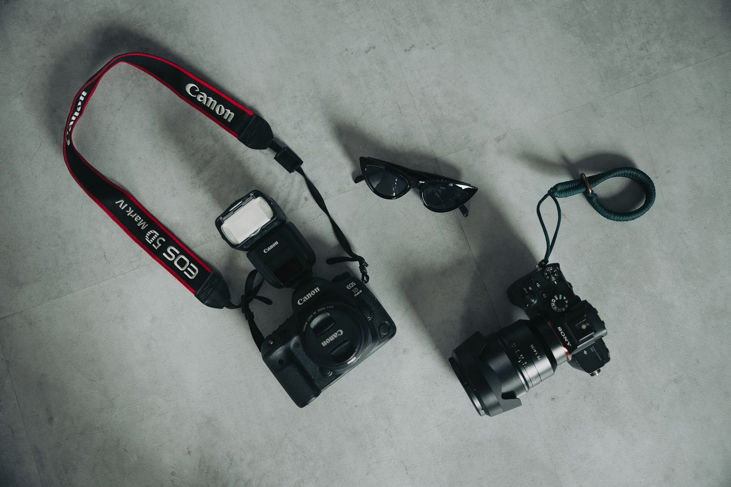 Two Canon DSLR cameras with straps and accessories laid flat on a gray concrete surface.
