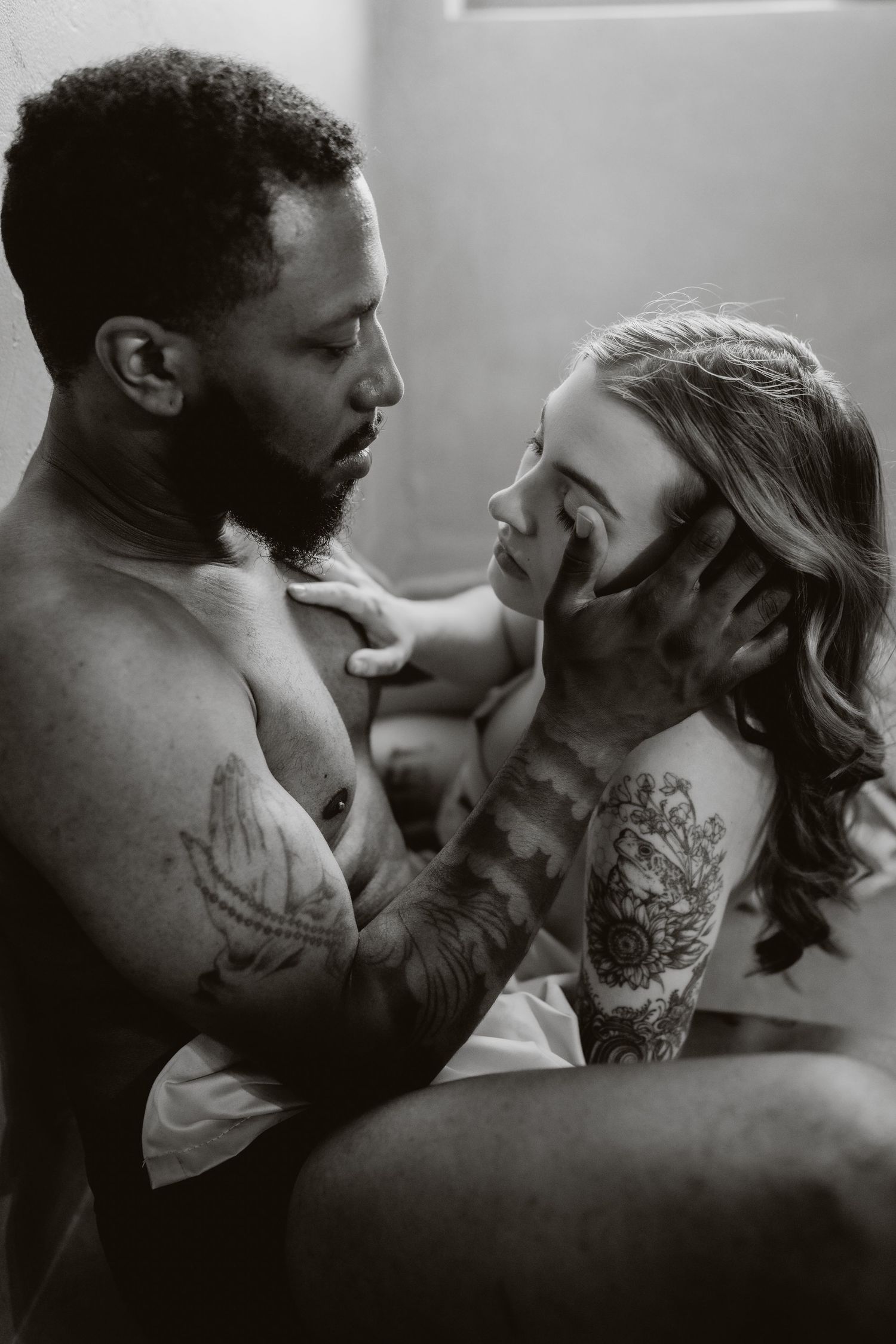 Black and white portrait of tattooed couple sharing an intimate moment in soft studio lighting.