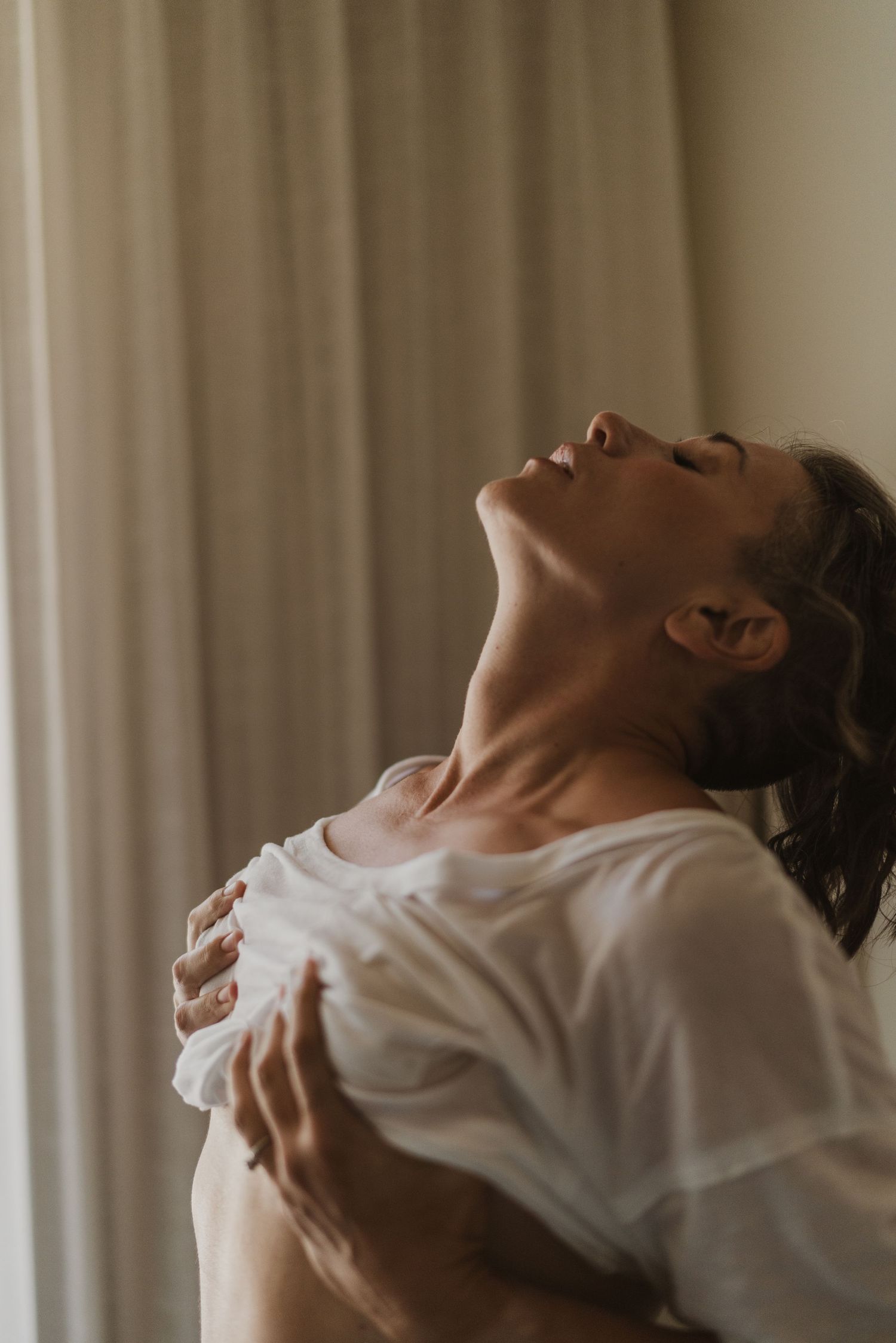 Woman in a white shirt with head tilted back and eyes closed in a serene pose.
