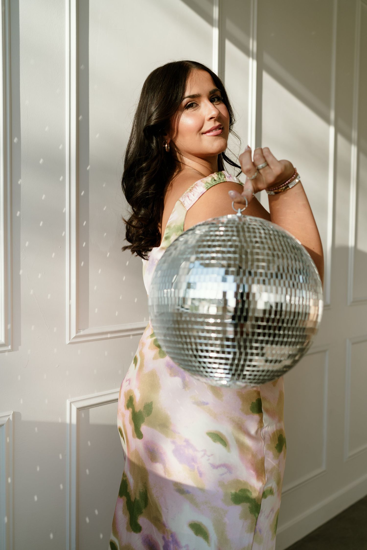 Woman in floral dress holding a disco ball against white wall.