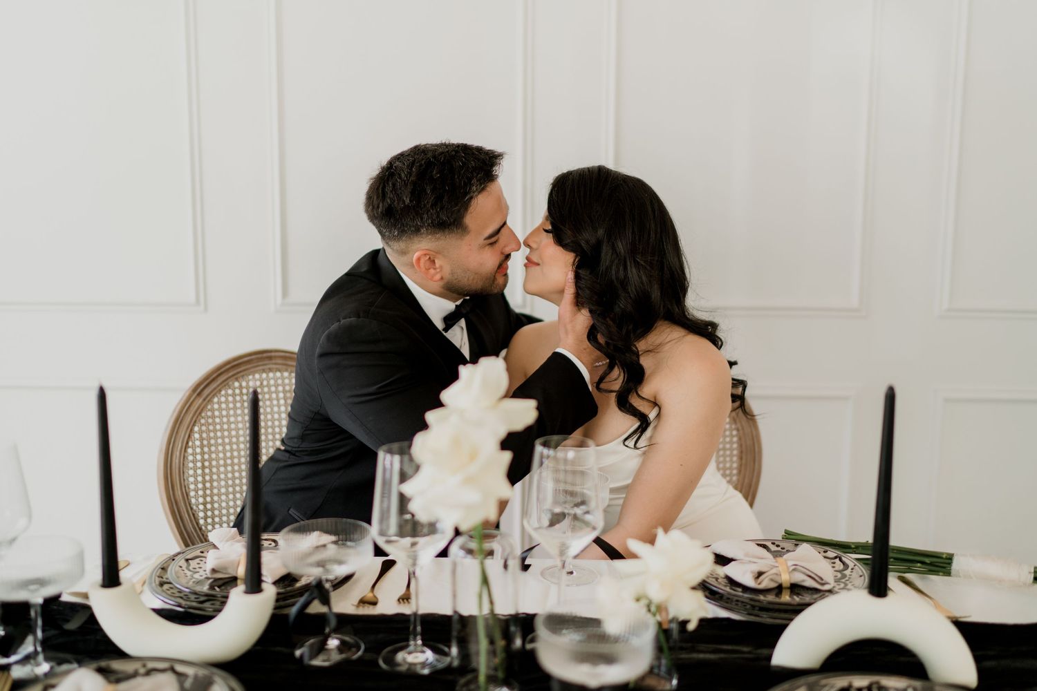 Bride and groom lean in for a kiss at decorated black and white wedding reception table.