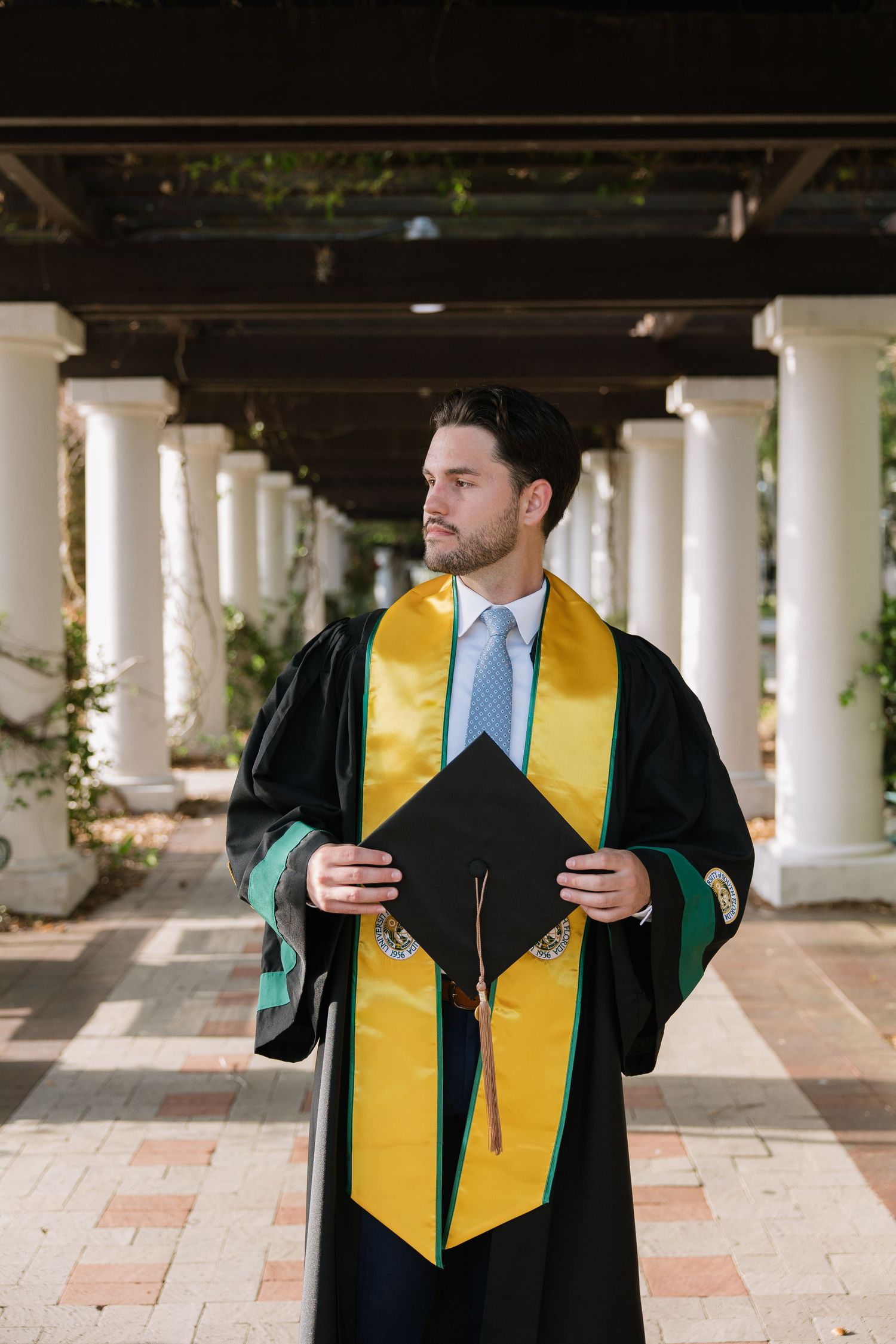 USF grad is in the pillars holding his cap for his graduation photos taken by Michaela Gom Photography.